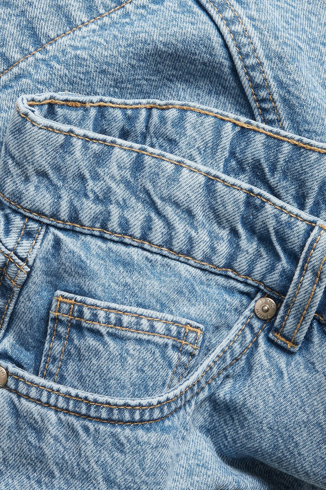 Närbild av en ljusblå A-linjeformad jeanskjol, med midjeband, framficka och silverfärgad knapp.