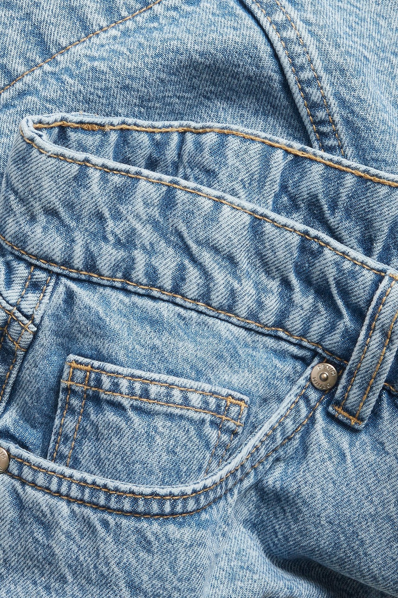 Närbild av en ljusblå A-linjeformad jeanskjol, med midjeband, framficka och silverfärgad knapp.