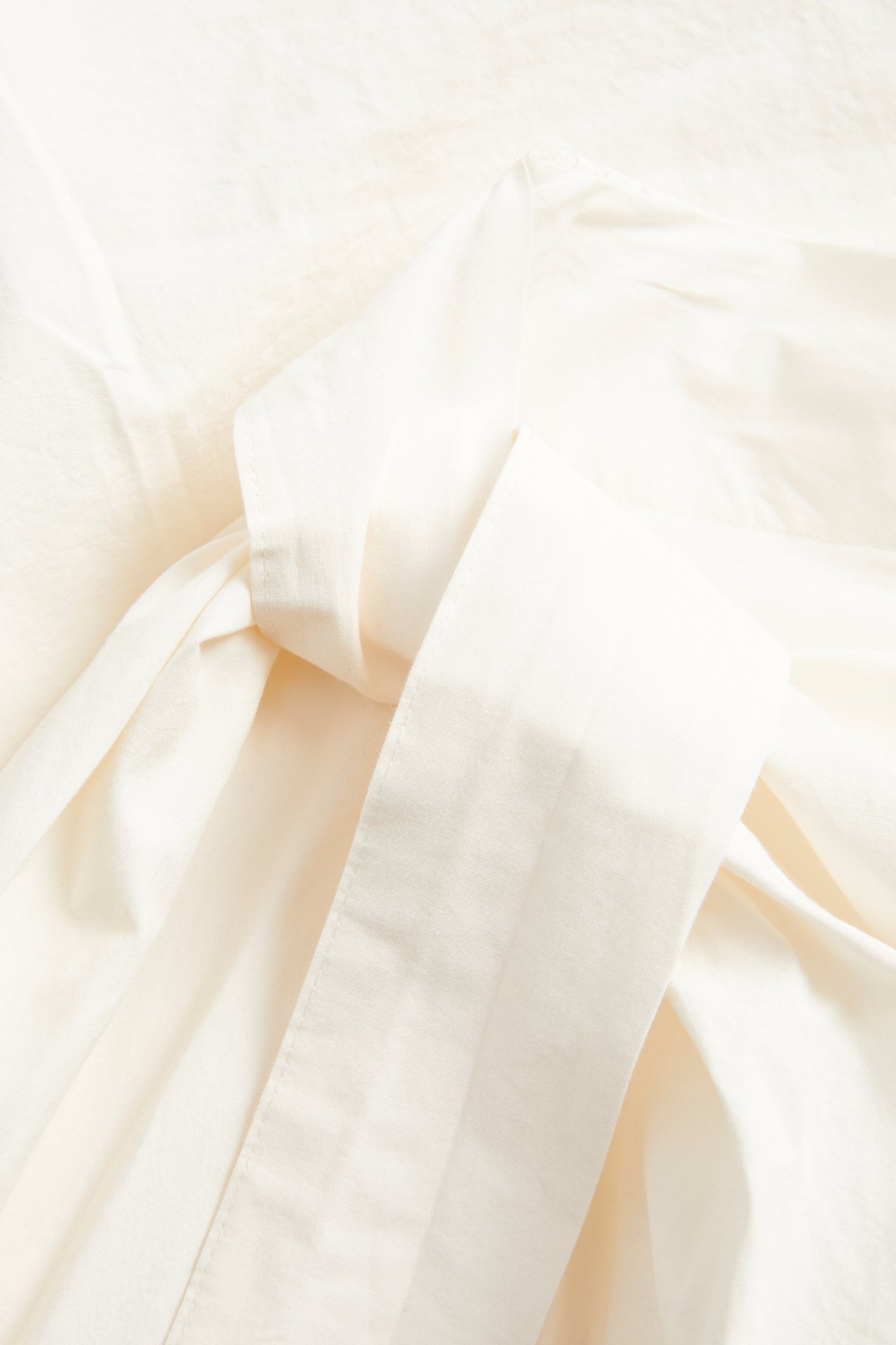 Lähikuva valkoisesta popliini-kietauluhameesta, jossa sivussa solmimisdetalji.