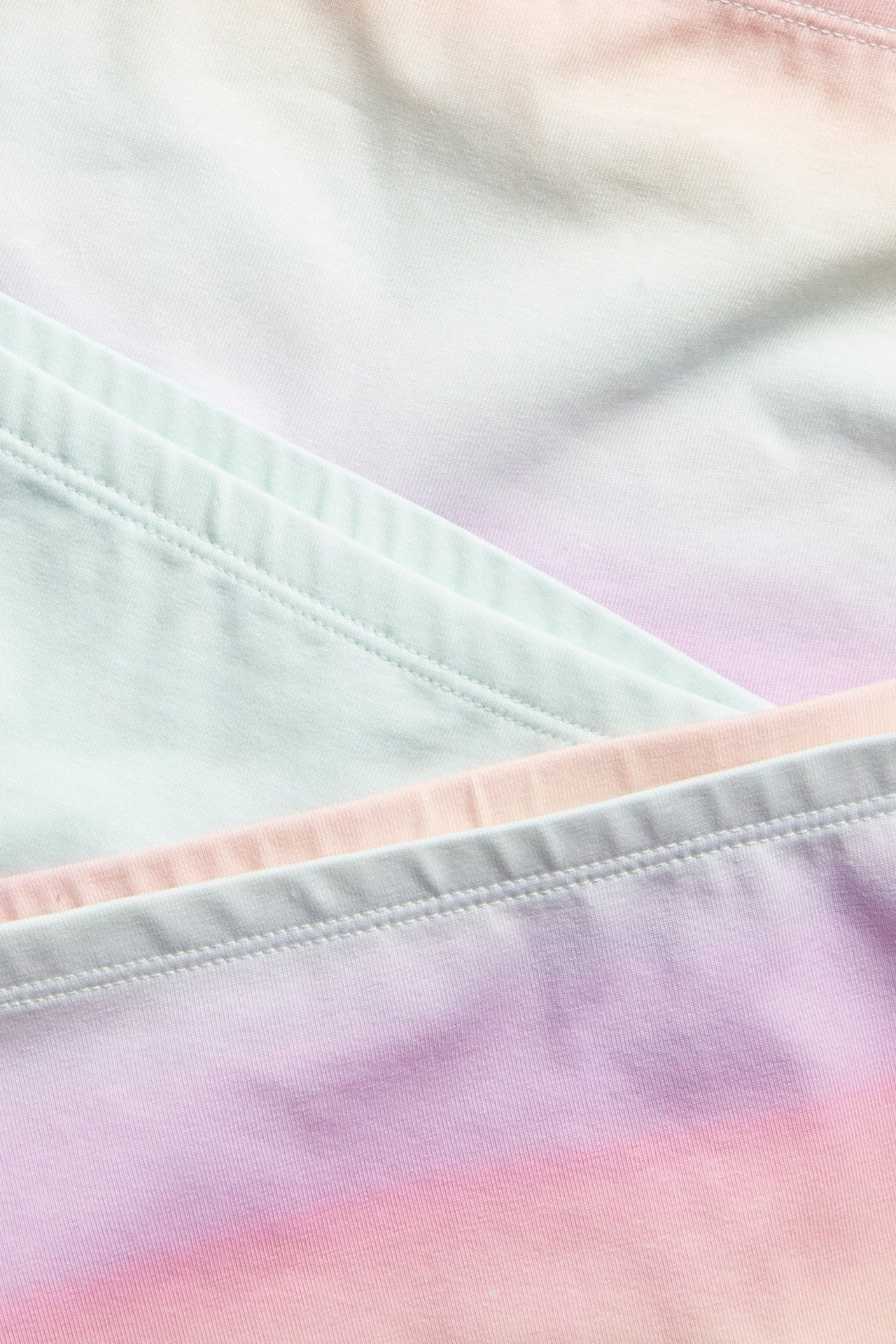 Lähikuva kolmesta pastellisävyisestä kuviollisesta puuvillabokserialushoususta; vaaleanpunainen, violetti ja mintunvihreä liukuvärjäys.