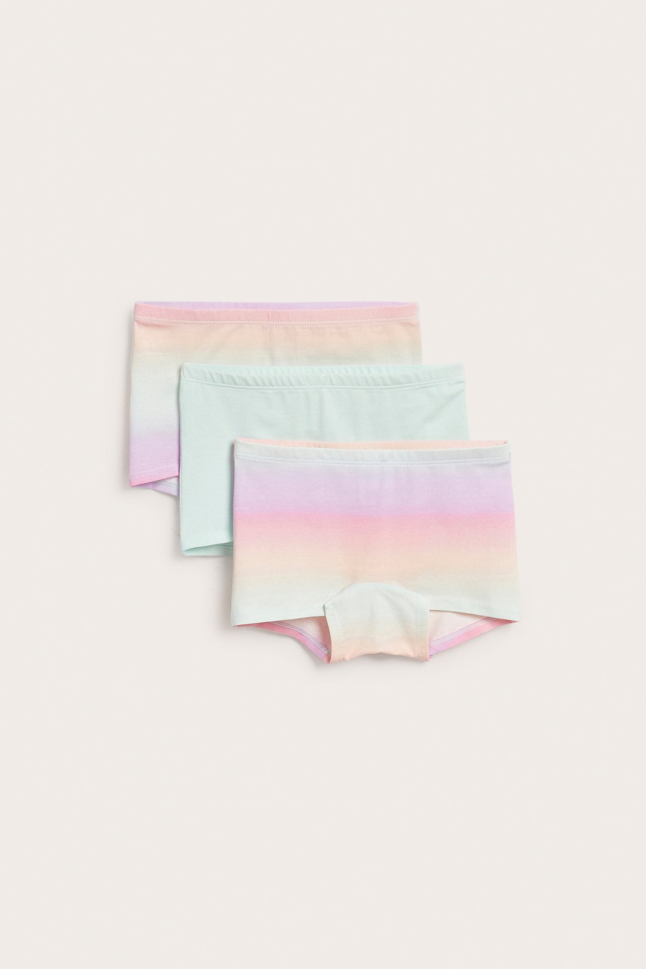 Ovenfra sett av tre myke boksertruser for barn med rosa, gul og lysegrønn ombré-mønster.