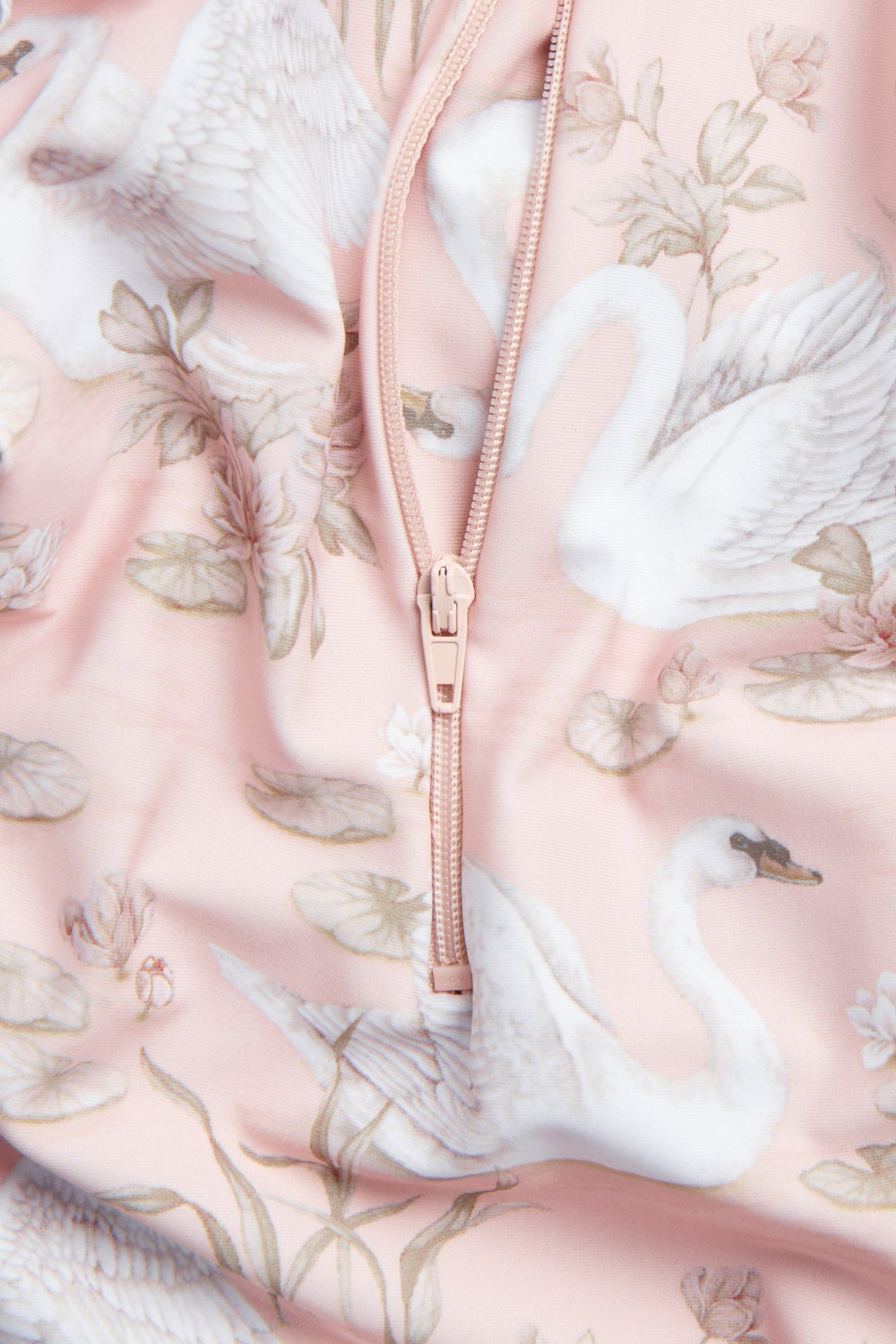 Närbild av en rosa UV-dräkt med vitt svan- och blommönster, med en dragkedja.