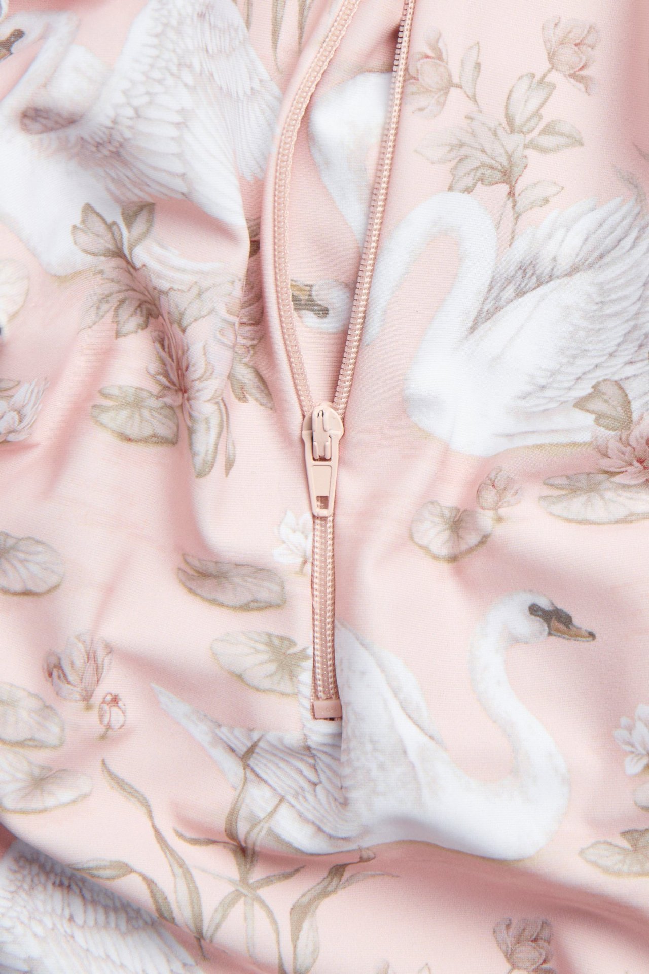 Nærbilde av en rosa UV-drakt med hvitt svane- og blomstermønster, med glidelås.