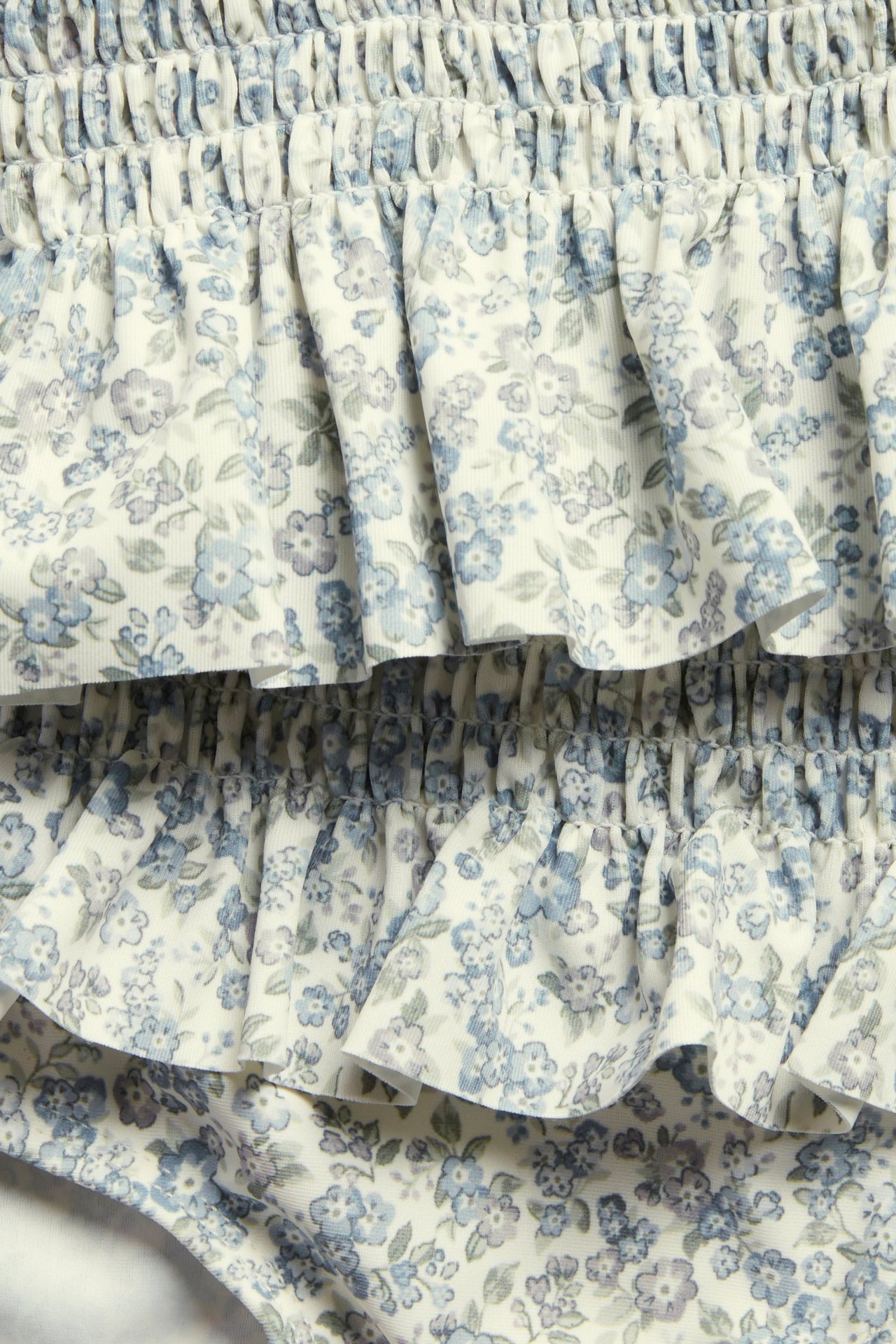 Närbild på en barnbikini med smock, volanger och ett småblommigt mönster i vitt och blått.