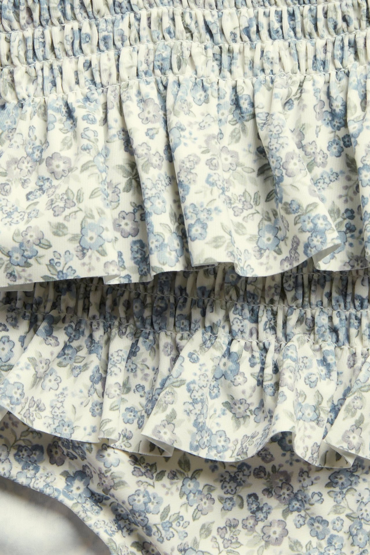 Zbliżenie na dziecięce bikini ze smockiem, falbankami i niebieskim wzorem w kwiaty na białym tle.