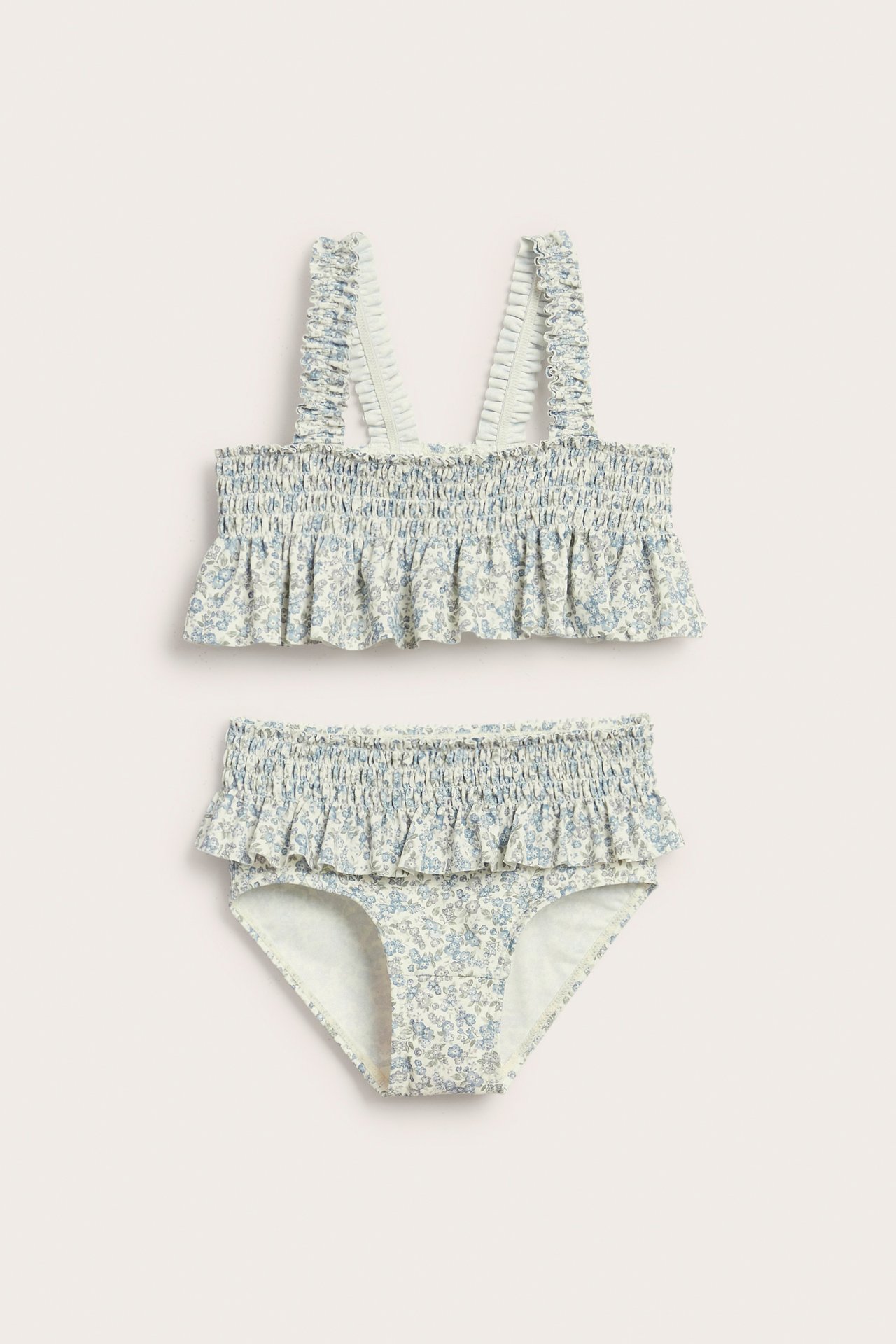 Framifrån: barnbikini med smockad topp och trosa i ljusblått/grönt blommönster, med volangprydda axelband.