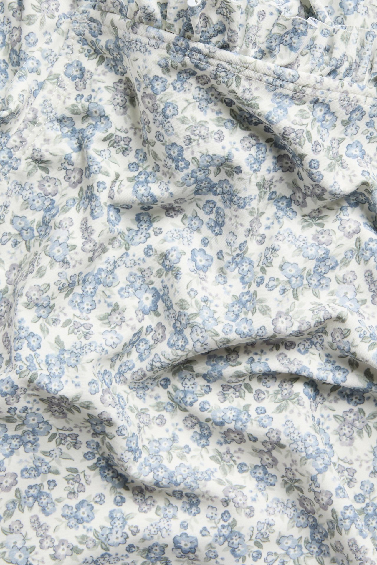 Zbliżenie: biały kostium kąpielowy dla niemowląt z niebiesko-zielonym wzorem kwiatowym i falbankami.