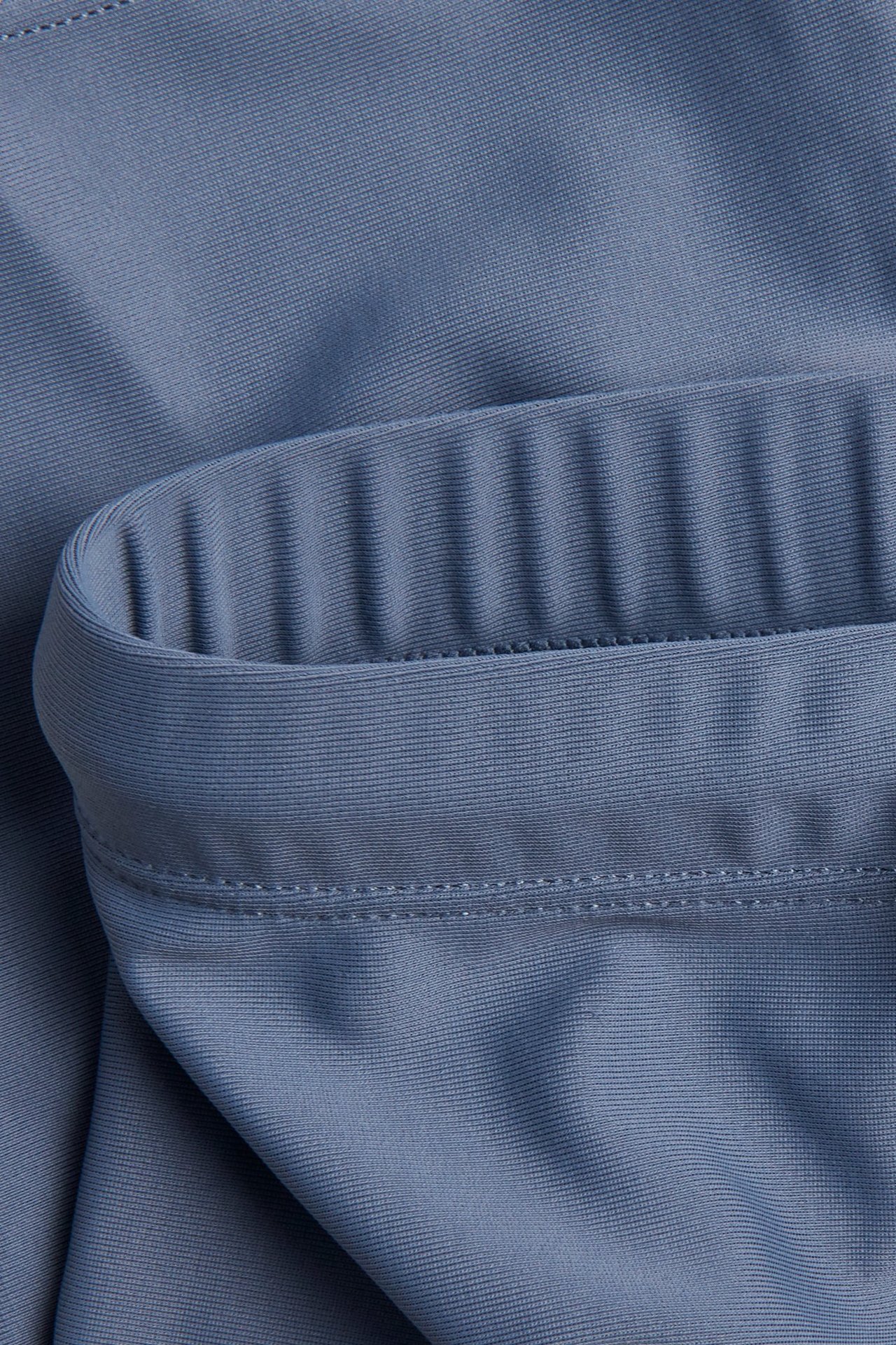 Närbild av enfärgade blå trekvarts UV-badbyxor med en ribbad resårdetalj.