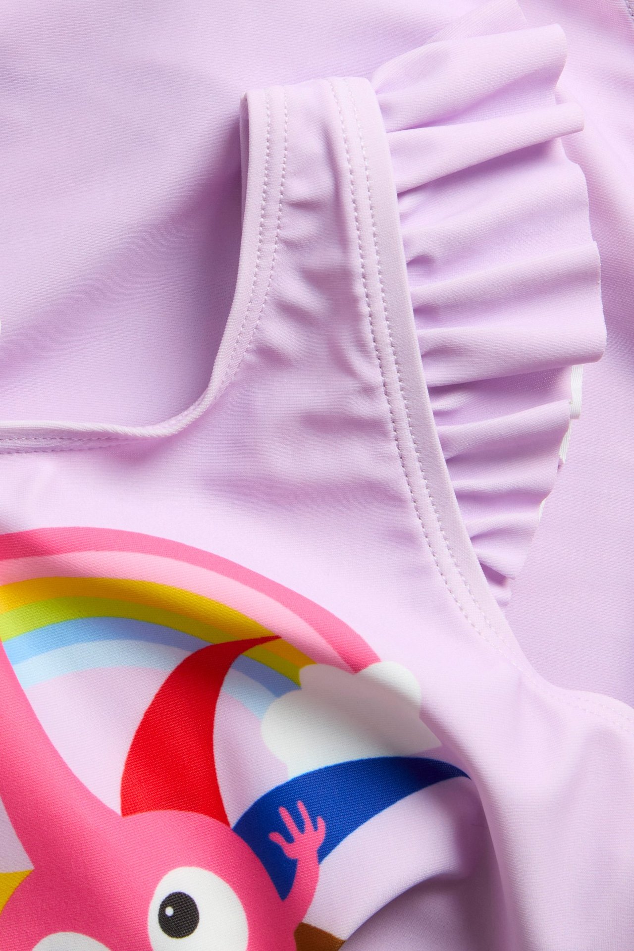 Zbliżenie: liliowy strój kąpielowy Babblarna dla dzieci z kolorowym nadrukiem i falbankami.