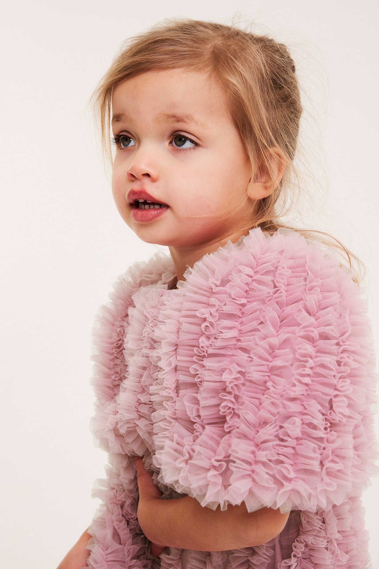 Nærbilde av et barn i en lyserosa volangkjole i mesh, med en knapp bak.