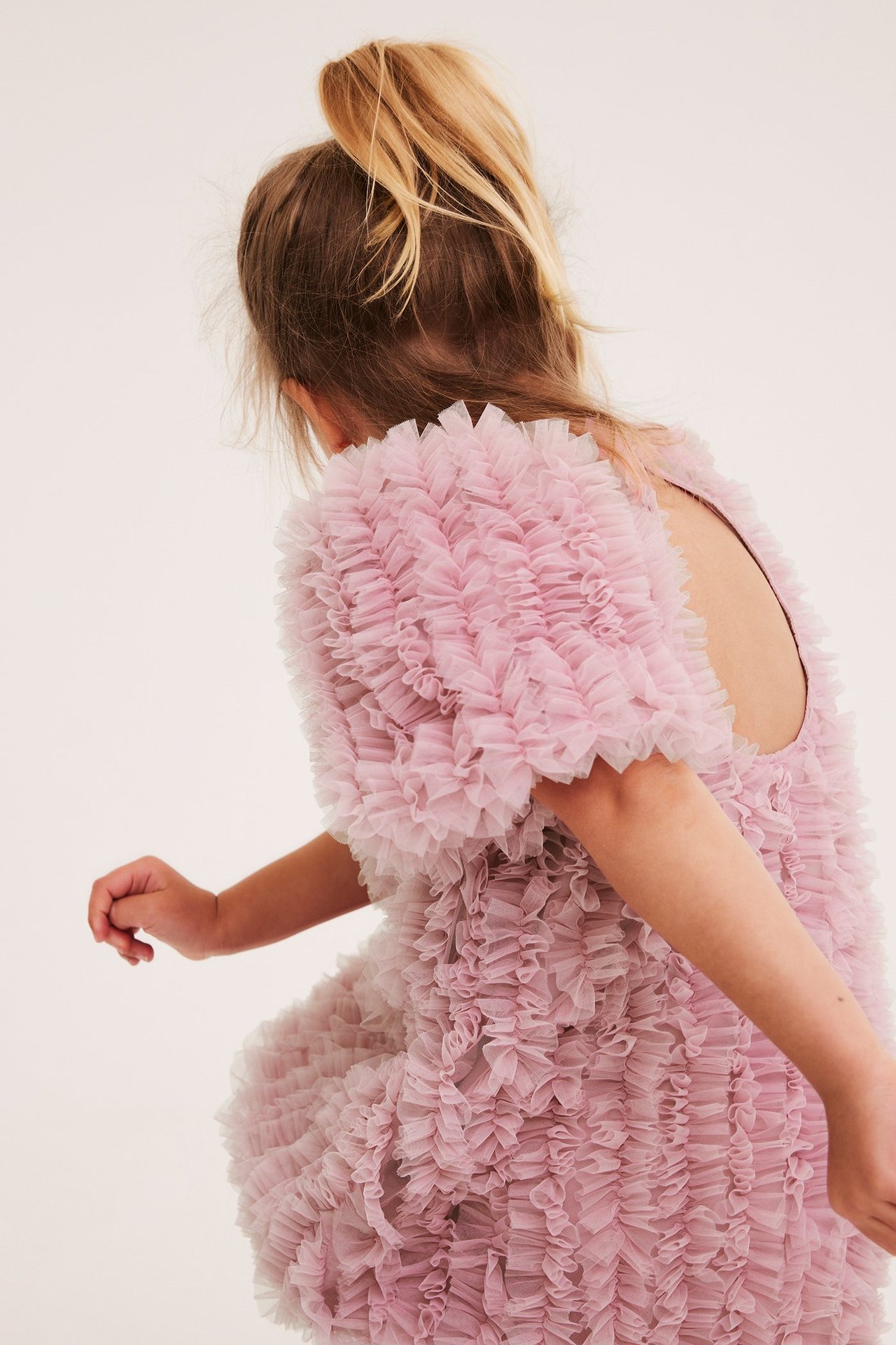 Barn i lyserosa rynket A-linjeformet meshkjole med nøkkelhullåpning bak, sett bakfra.