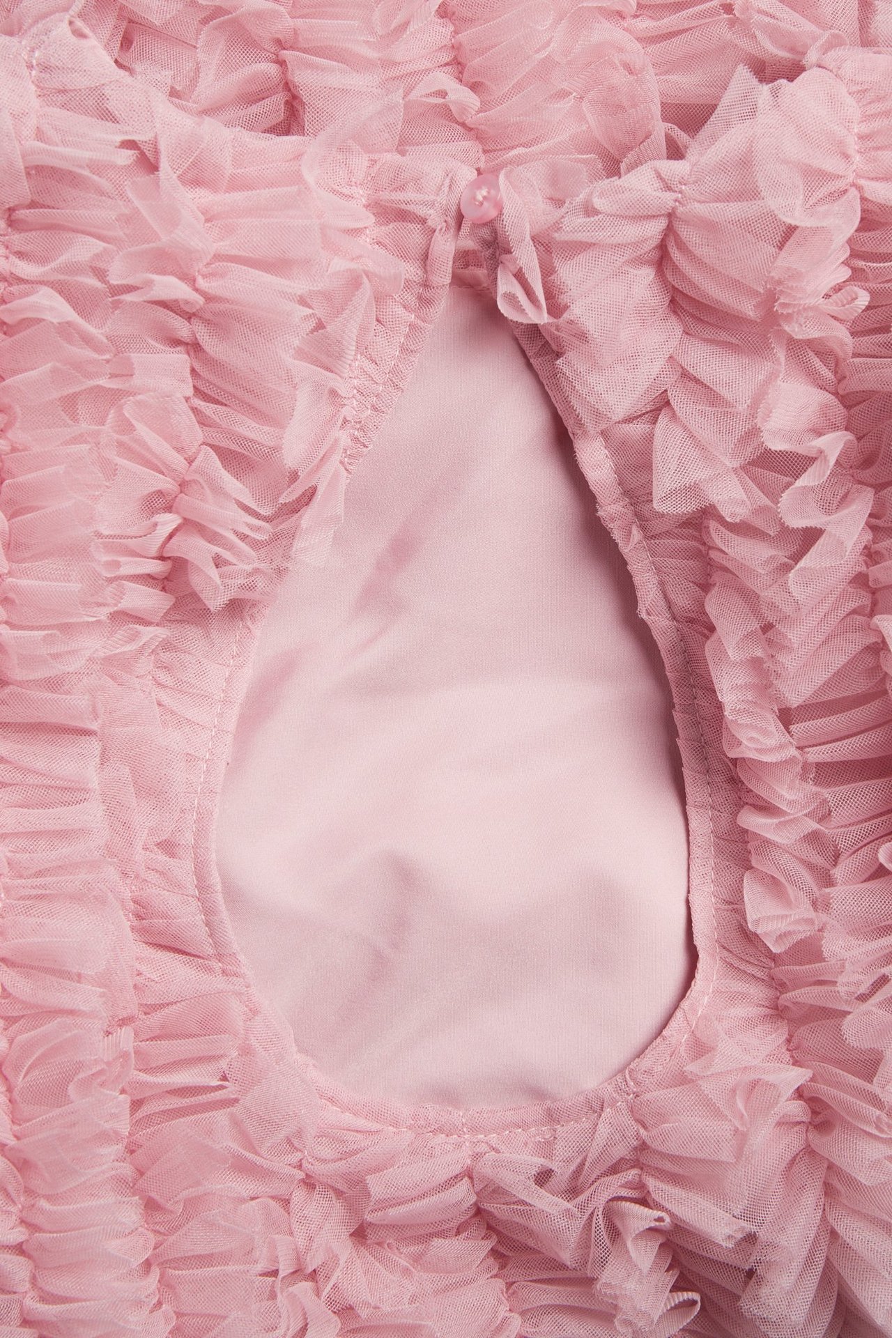 Zbliżenie, widok z tyłu: jasnoróżowa sukienka dziecięca z falbankami z siateczki, z rozcięciem i zapięciem na guzik.