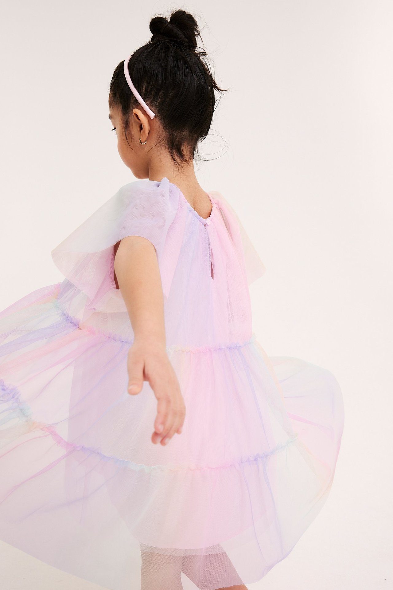 Bakifrån på ett barn i en voluminös, regnbågsfärgad tyllklänning med puffärmar och rosa hårband.