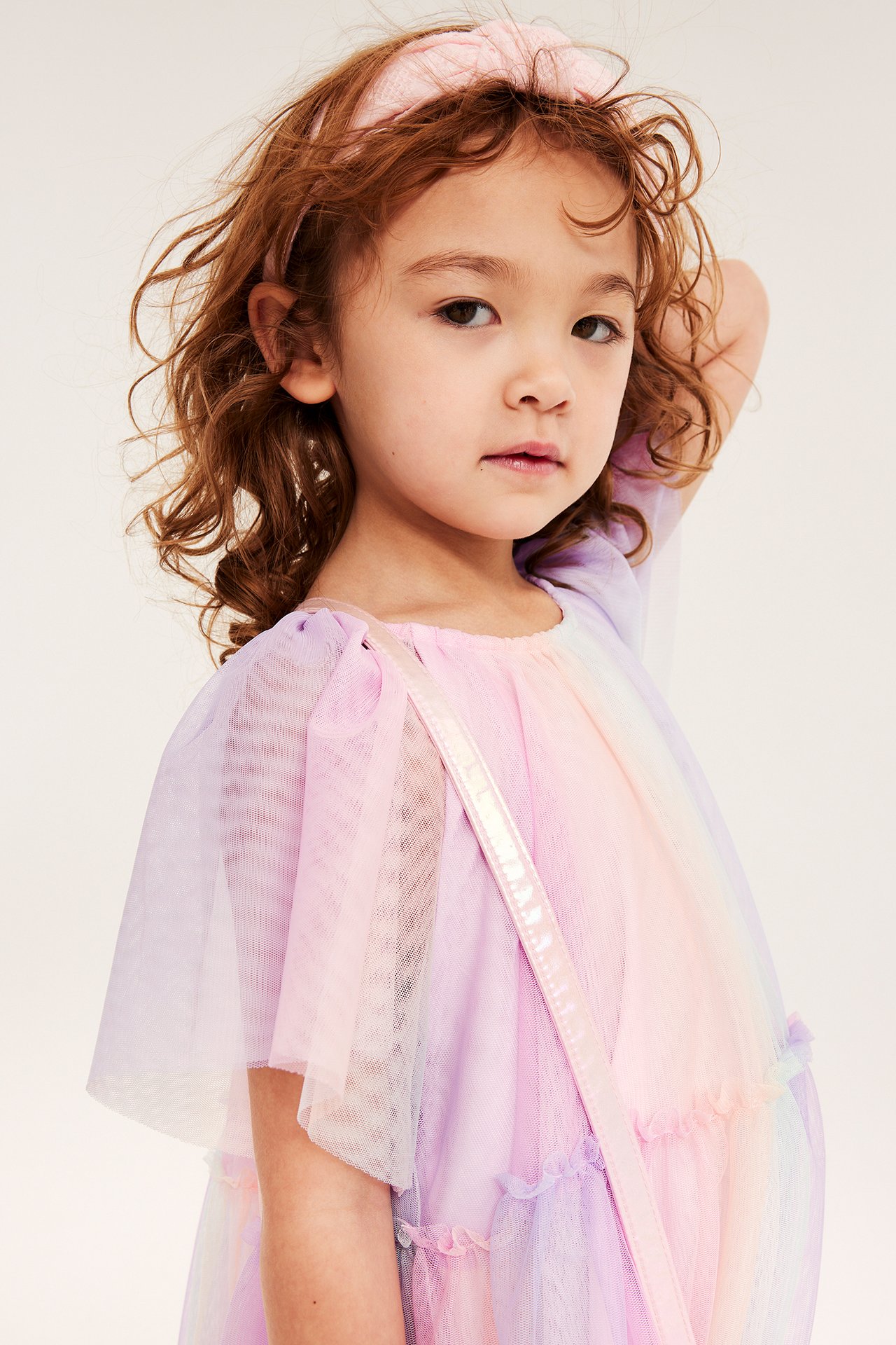 Lapsi sateenkaarenvärisessä tyllimekossa, vaaleanpunaisessa hiuspannassa ja vaaleanpunaisessa olkalaukussa.