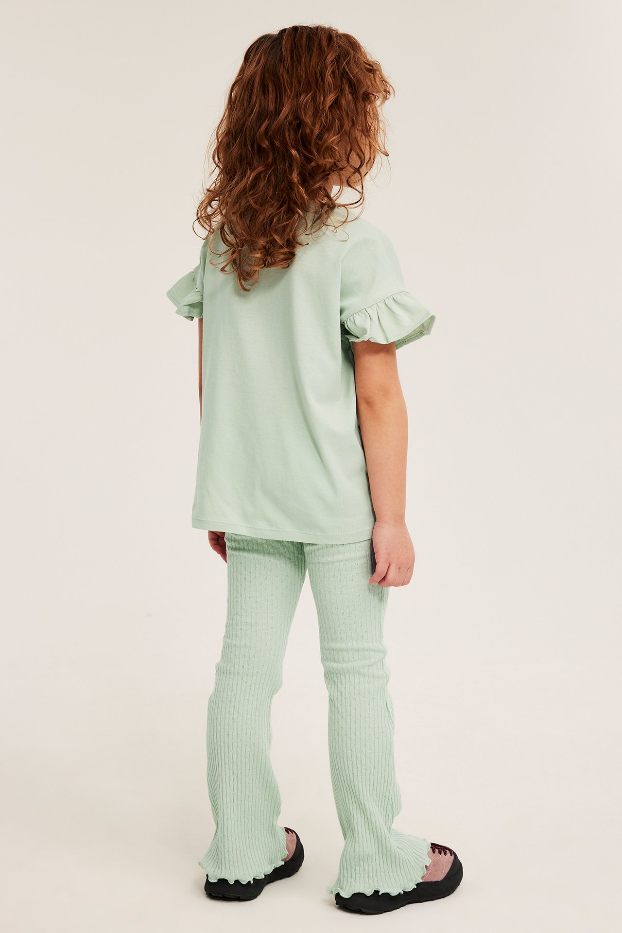 Bakifrån: Barn i ljusgröna ribbstickade utsvängda leggings med babylock och matchande volang-t-shirt.