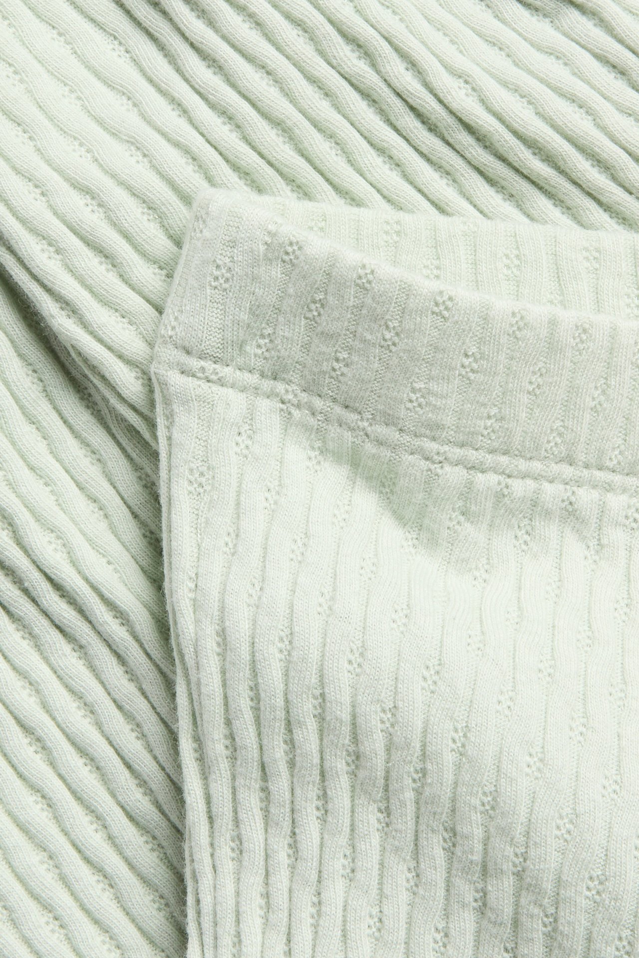 Närbild på ljusgröna strukturmönstrade utsvängda leggings, visar ribbat mönster och midjeresår.