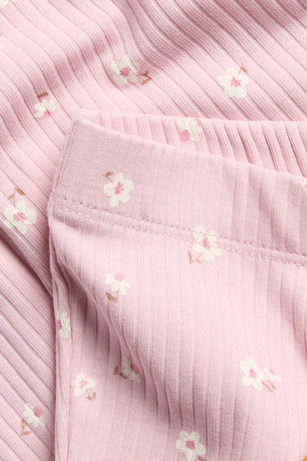 Zbliżenie jasnoróżowych prążkowanych legginsów bawełnianych z drobnym kwiatowym wzorem i elastycznym pasem.