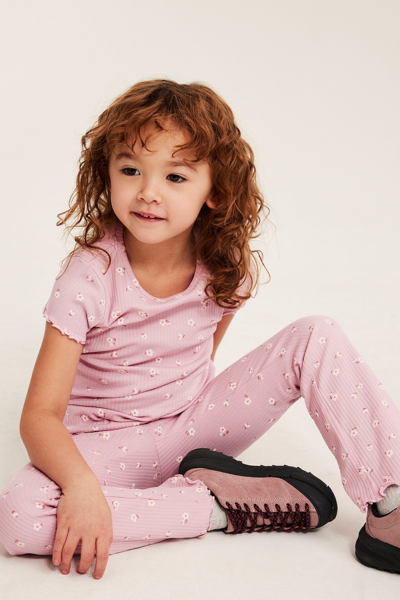 Widok z przodu dziecka w jasnoróżowych ryflowanych legginsach dzwonach, pasującym topie i różowych butach.