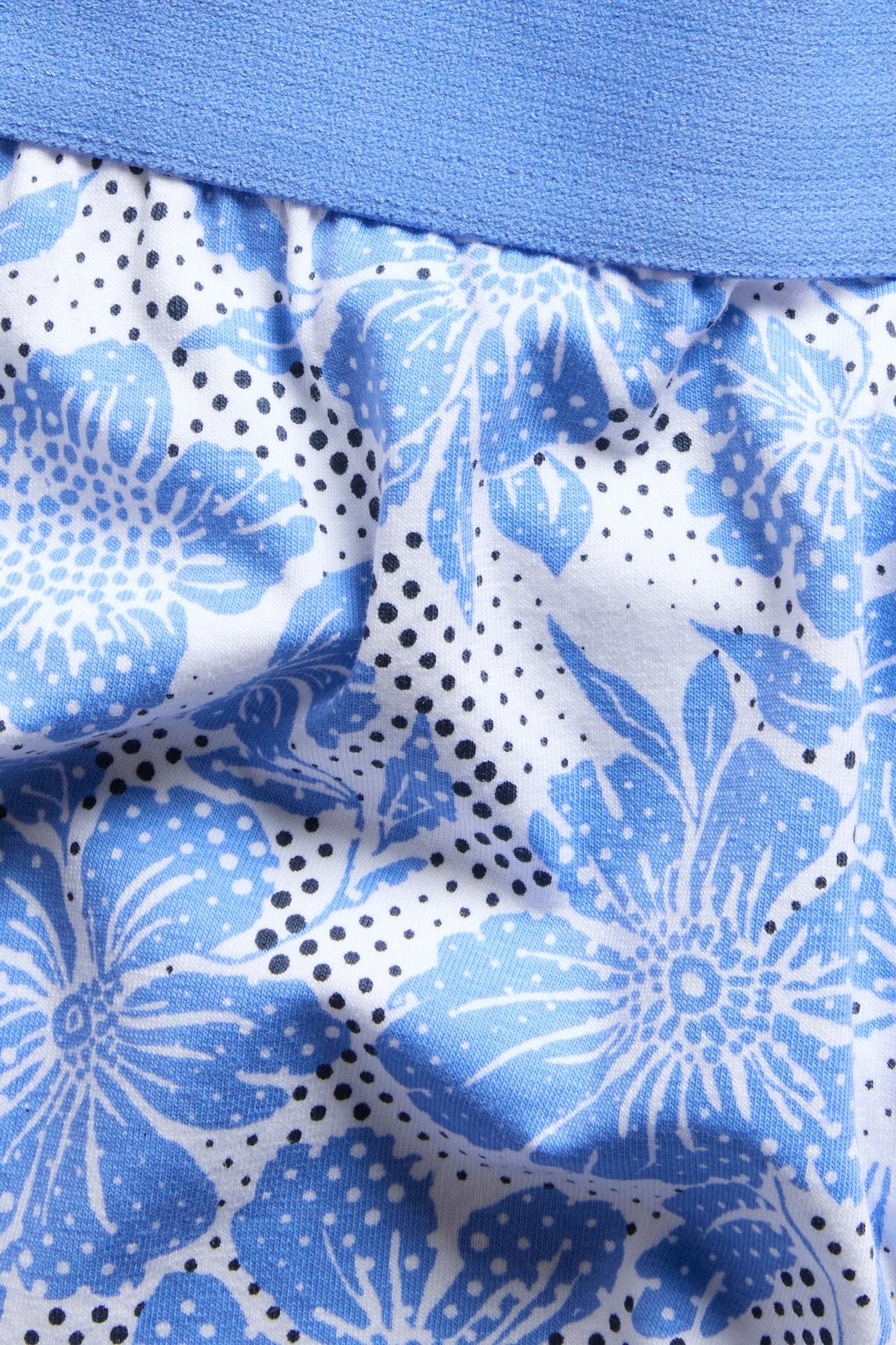 Zbliżenie męskich niebieskich bokserek w kwiaty z niebieskim pasem i czarnymi kropkami.