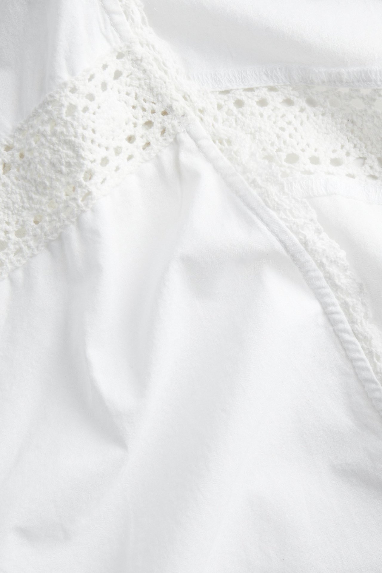 Närbild av vit bomullsblus med spetsdetaljer över bröstet.