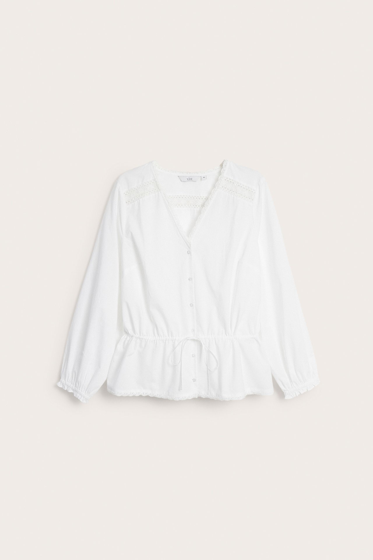 Framifrån, vit bomullsblus med spetsdetaljer, dragsko i midjan och resår i ärmsluten.
