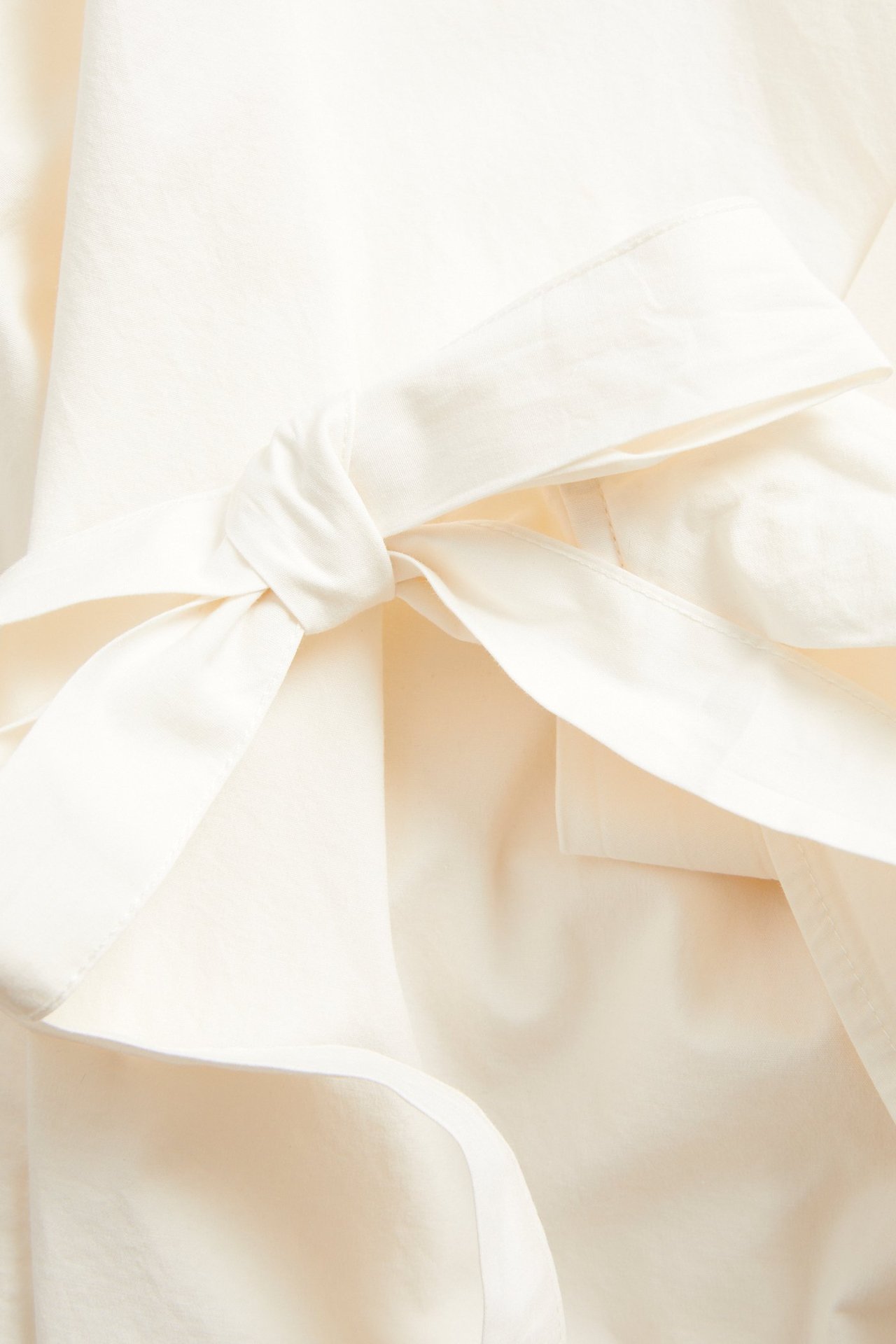Lähikuva valkoisesta kudotusta popliinista valmistetusta kietaisupuserosta, jossa on solmittava yksityiskohta sivulla.