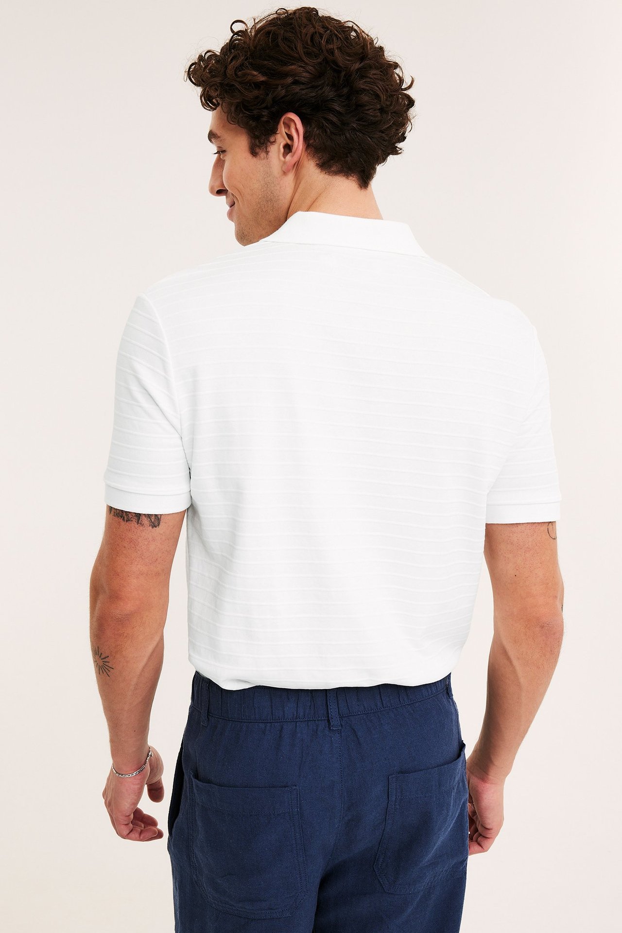 Takakuva: mies yllään valkoinen raidallinen lyhythihainen pikeepaita ja tummansiniset joustovyötäröhousut.