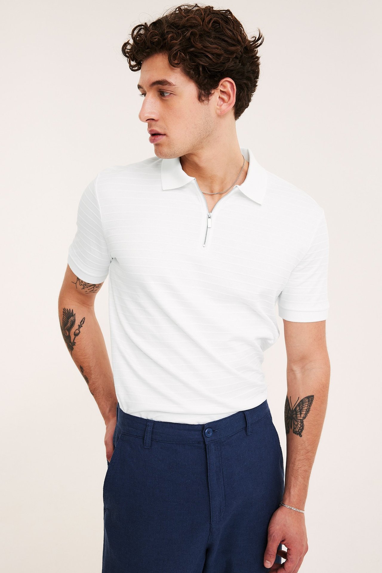 Sidovy av en man i en vit kortärmad pikétröja med dragkedja och mörkblå shorts.