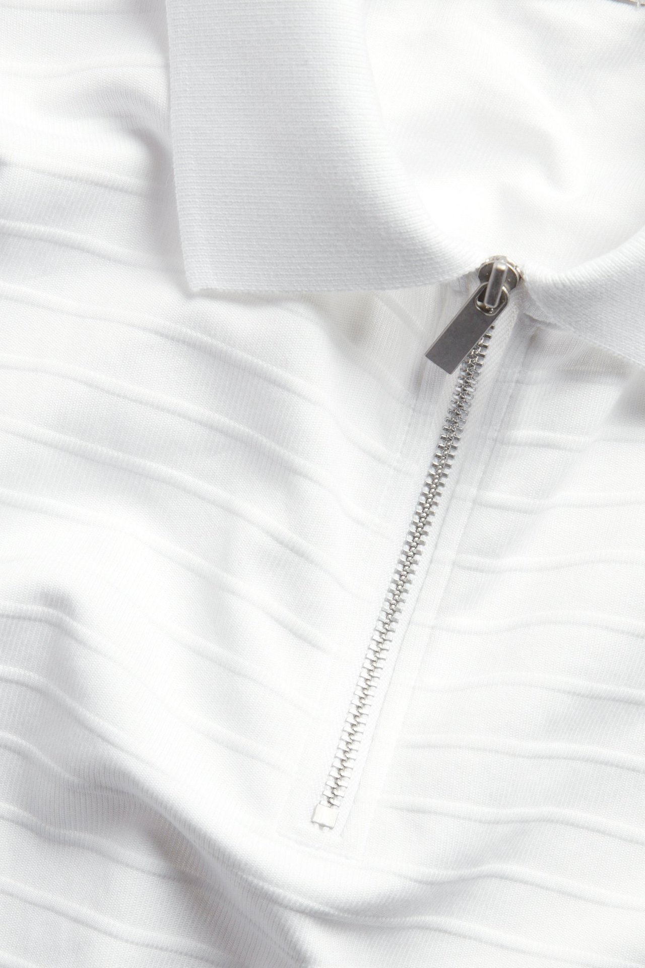 Närbild av en vit texturerad pikétröja med krage och silverdragkedja framtill.