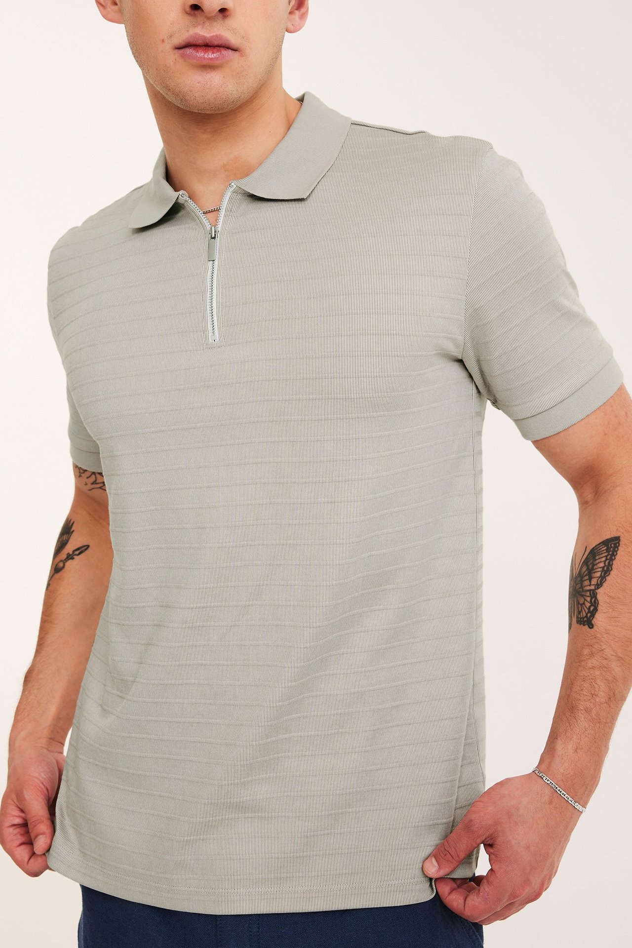 Lähikuva miehestä yllään beige lyhythihainen pikeepaita vetoketjulla ja vaakasuuntaisilla kuvioiduilla raidoilla.