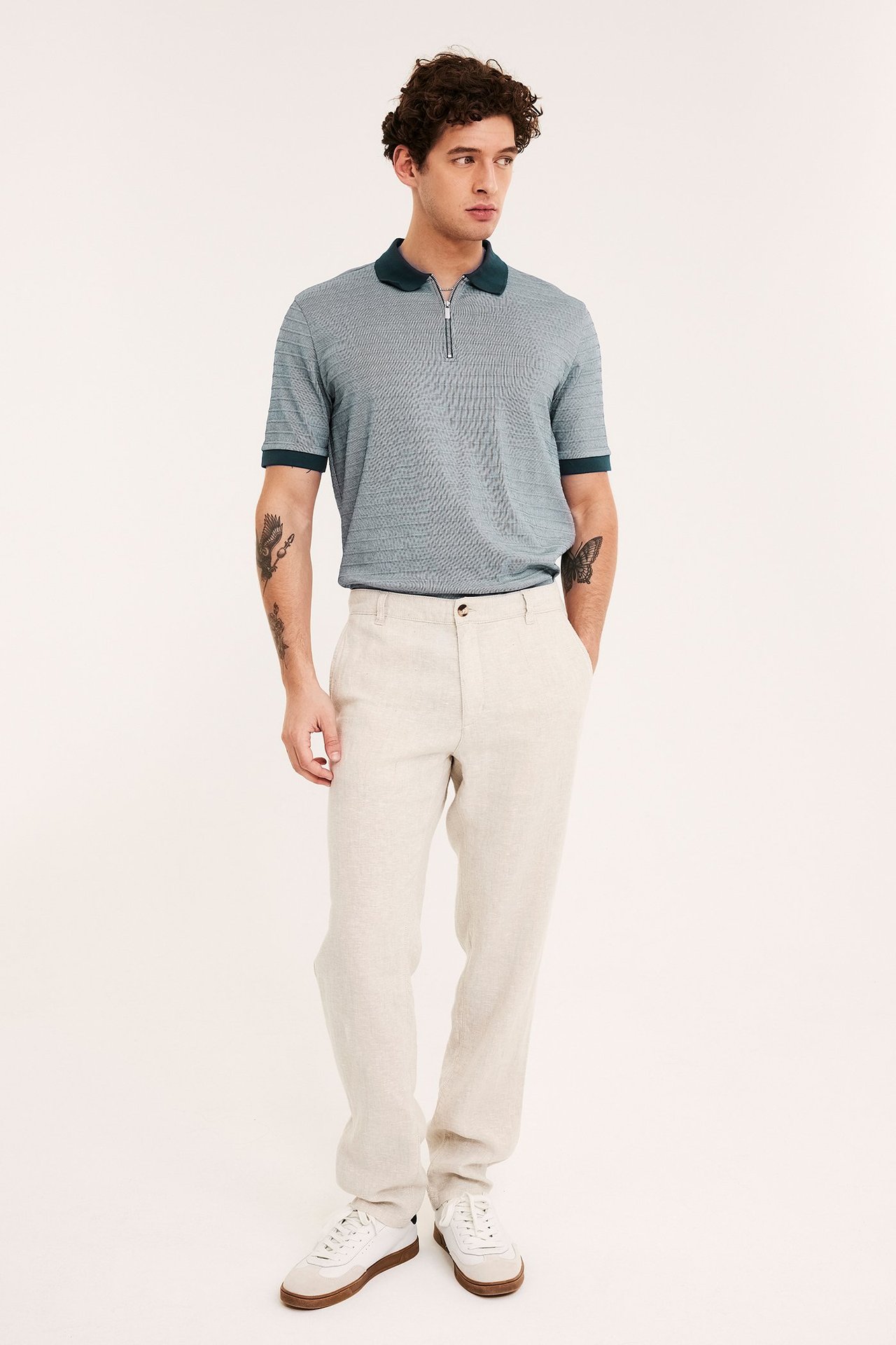 Framifrån: man i mörkblå pikétröja med dragkedja, ljusbeige byxor och vita sneakers.