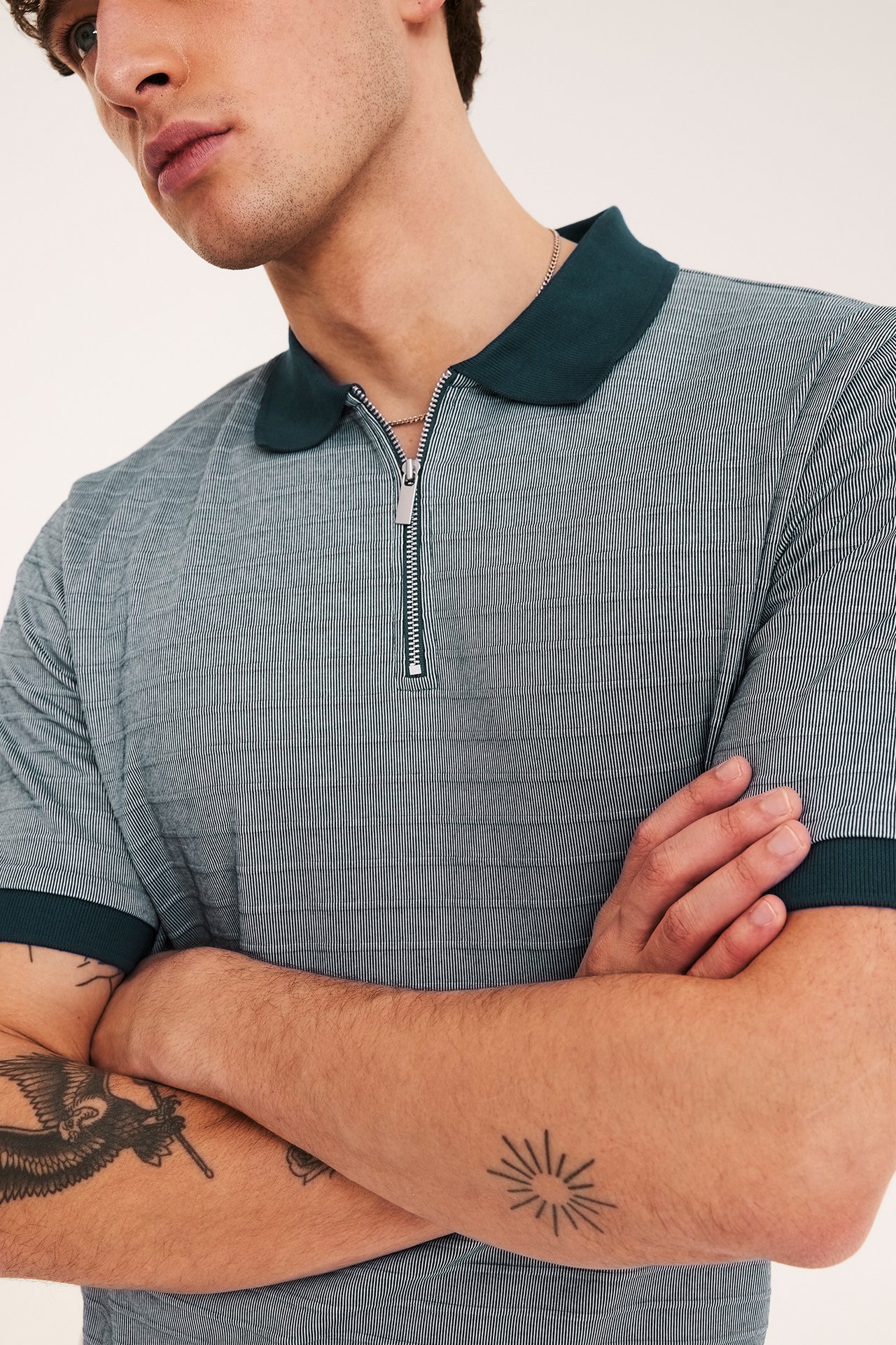 Lähikuva miehestä yllään raidallinen pikeepaita, jossa tummansininen kaulus, hihansuut ja vetoketju.