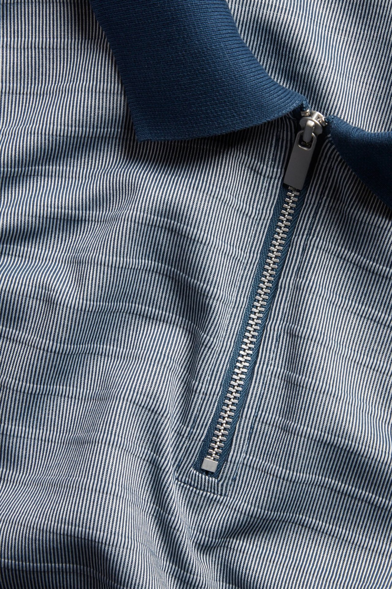 Närbild på en blåvitrandig pikétröja med mörkblå pikékrage och silverdragkedja.