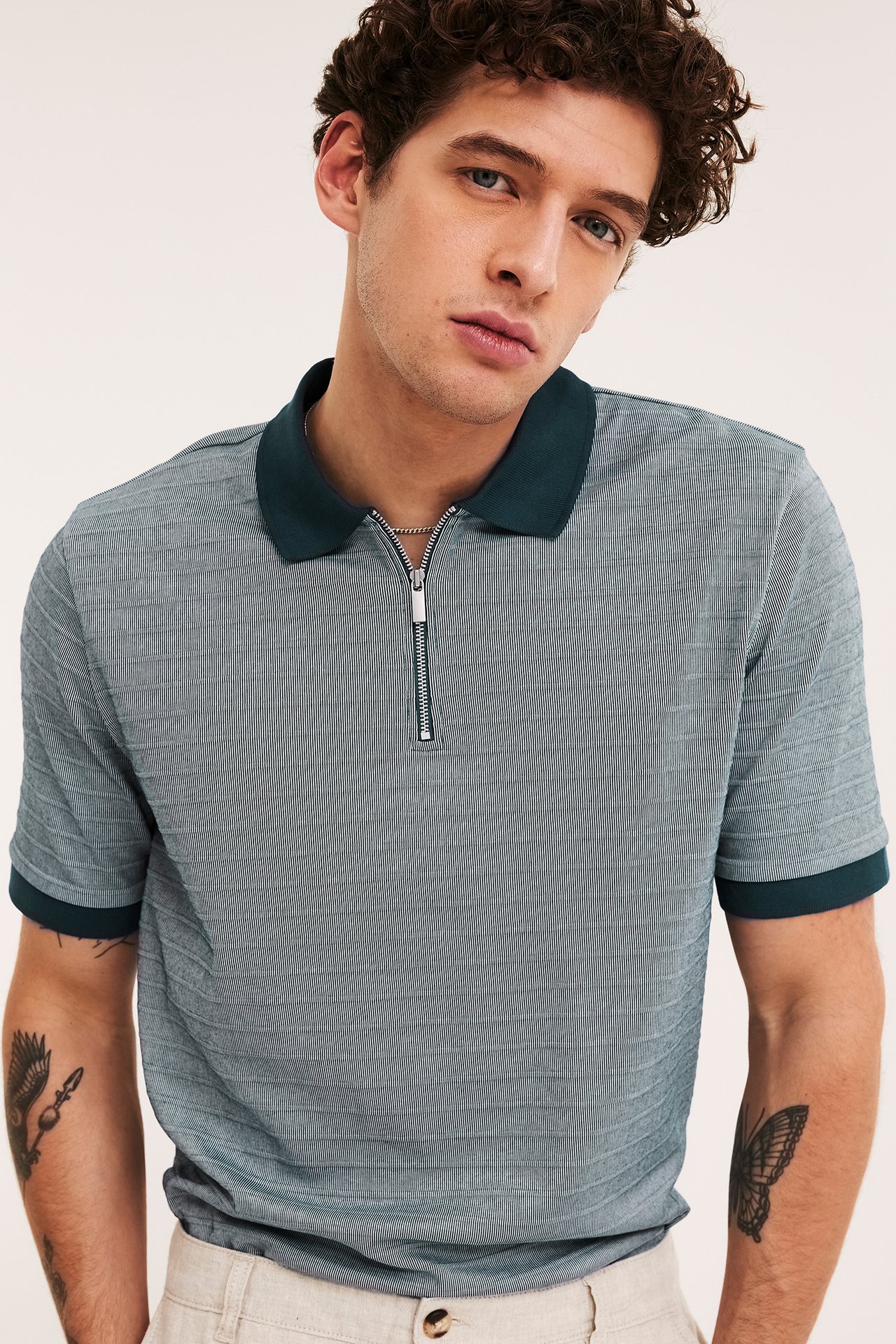 Edestäpäin mies yllään harmaansininen kuvioitu pikeepaita tummanvihreällä kauluksella ja vetoketjulla.