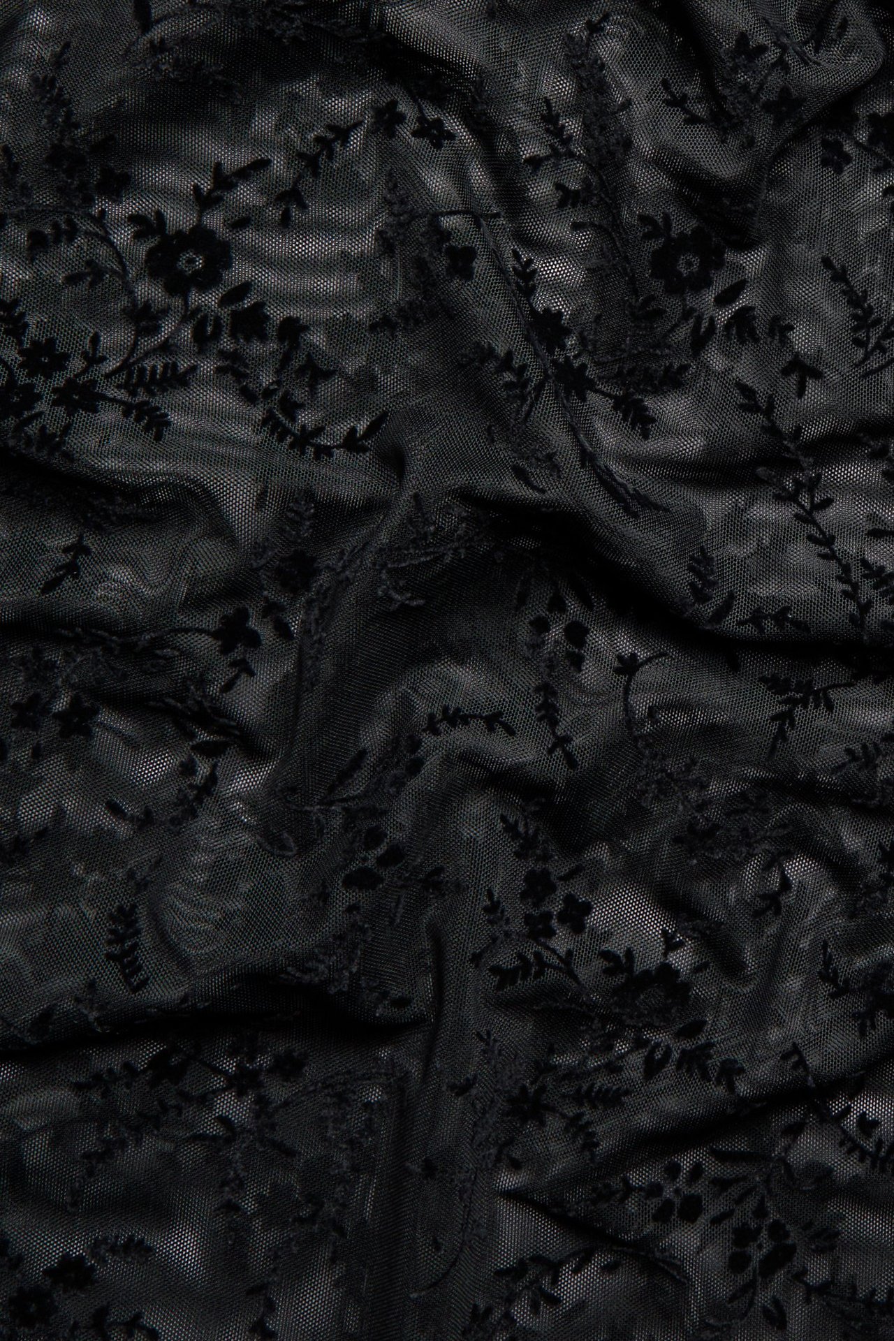 Zbliżenie czarnego, przezroczystego materiału na bluzkę z długim rękawem z welurowym wzorem w kwiaty.