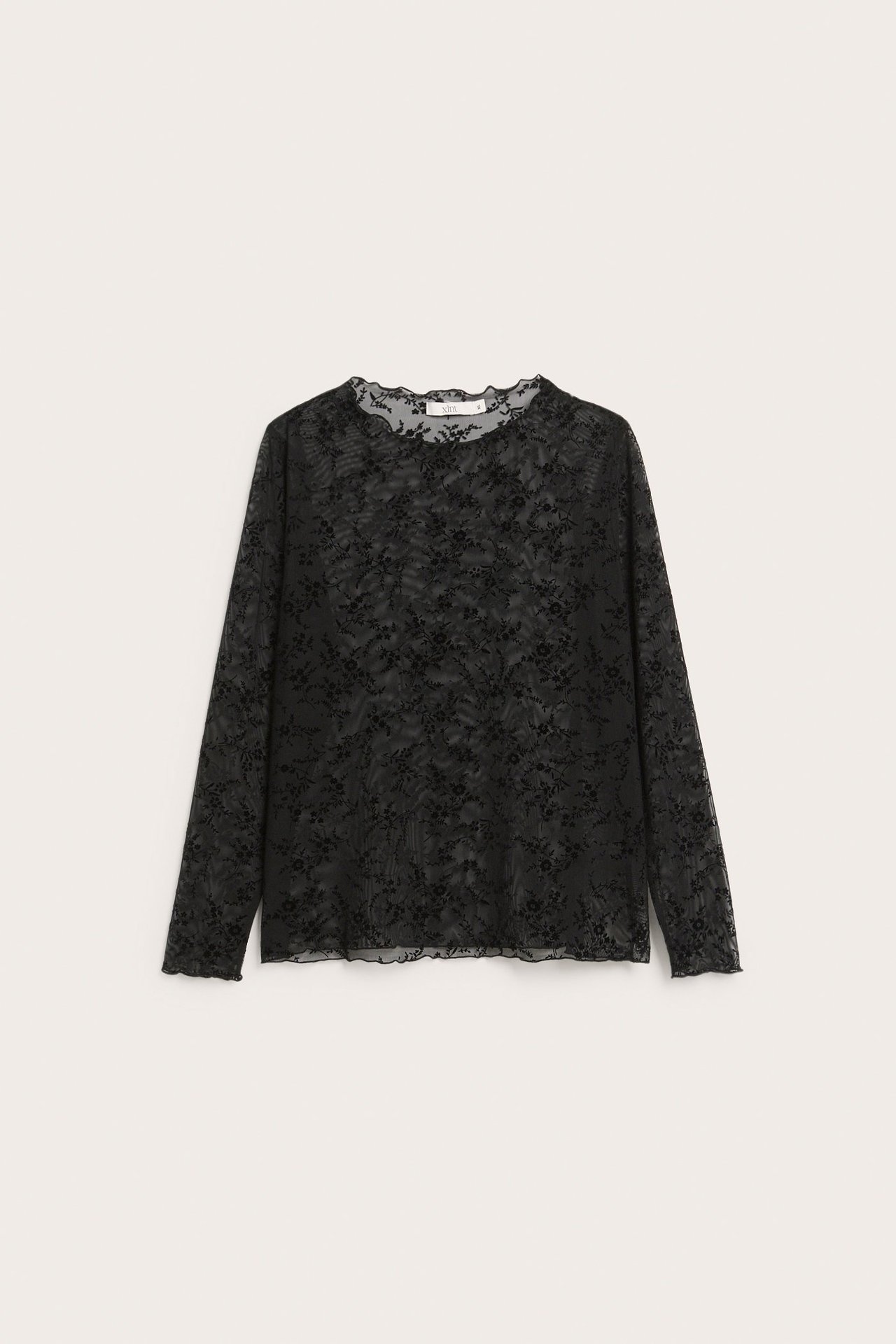 Frontvy av en svart långärmad topp i flockat tyg med blommönster och volangkanter.