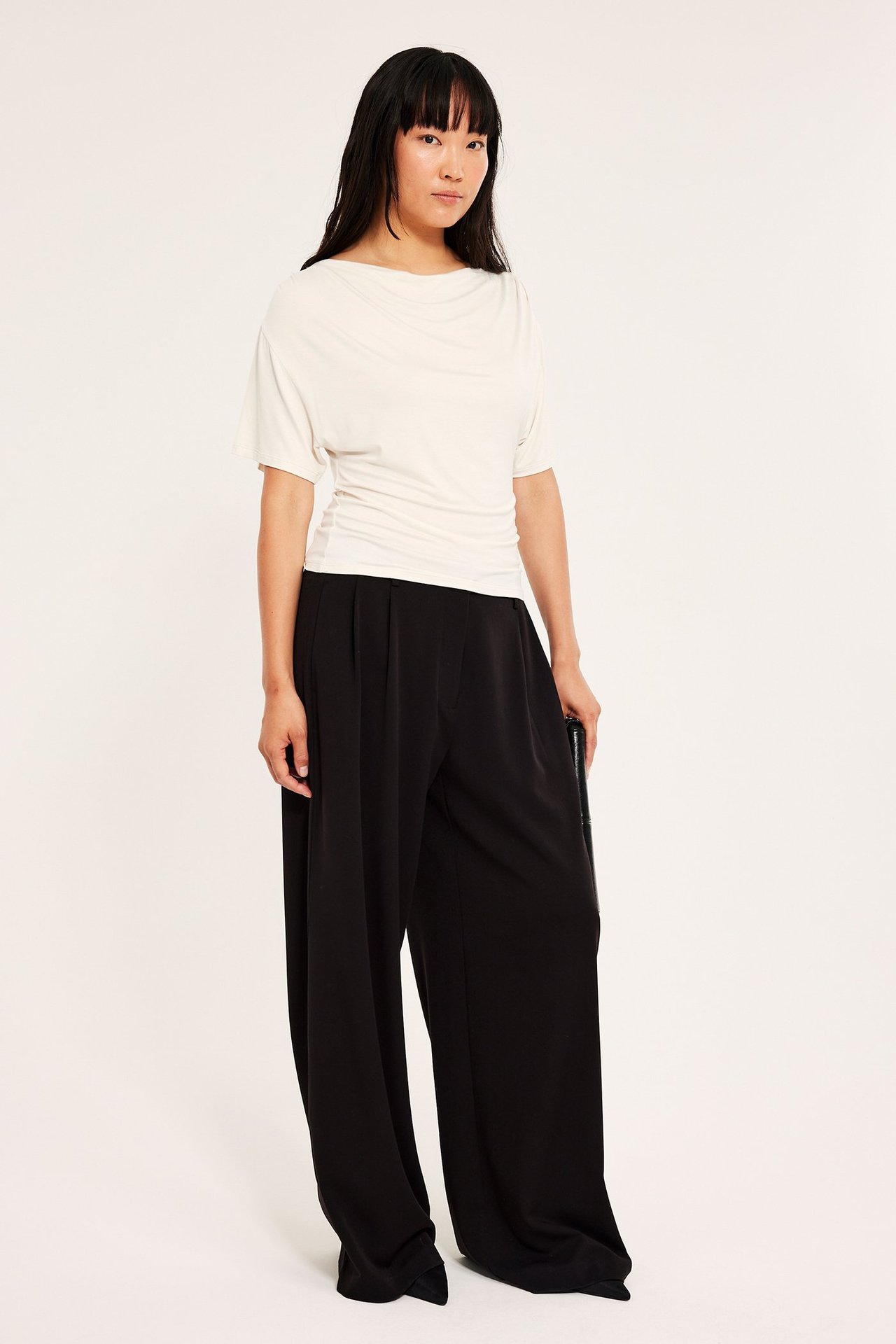 Offwhite kortermet viskosebluse med drapering, kvinner bruker den over svarte bukser.