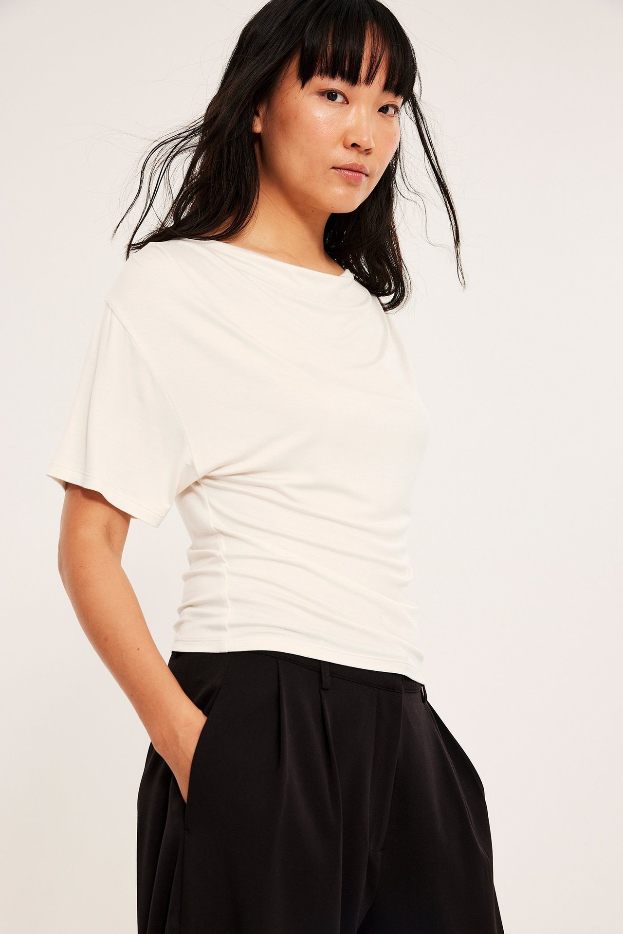 Kvinne i offwhite kortermet viskose topp med drapering, svarte bukser, frontperspektiv.