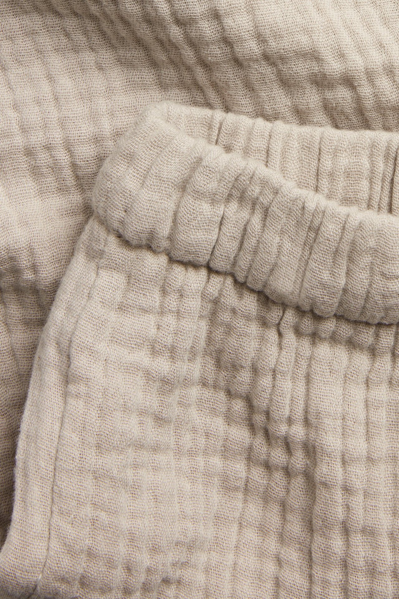 Nærbilde av beige vevde muslinbukser til baby med elastisk midje.