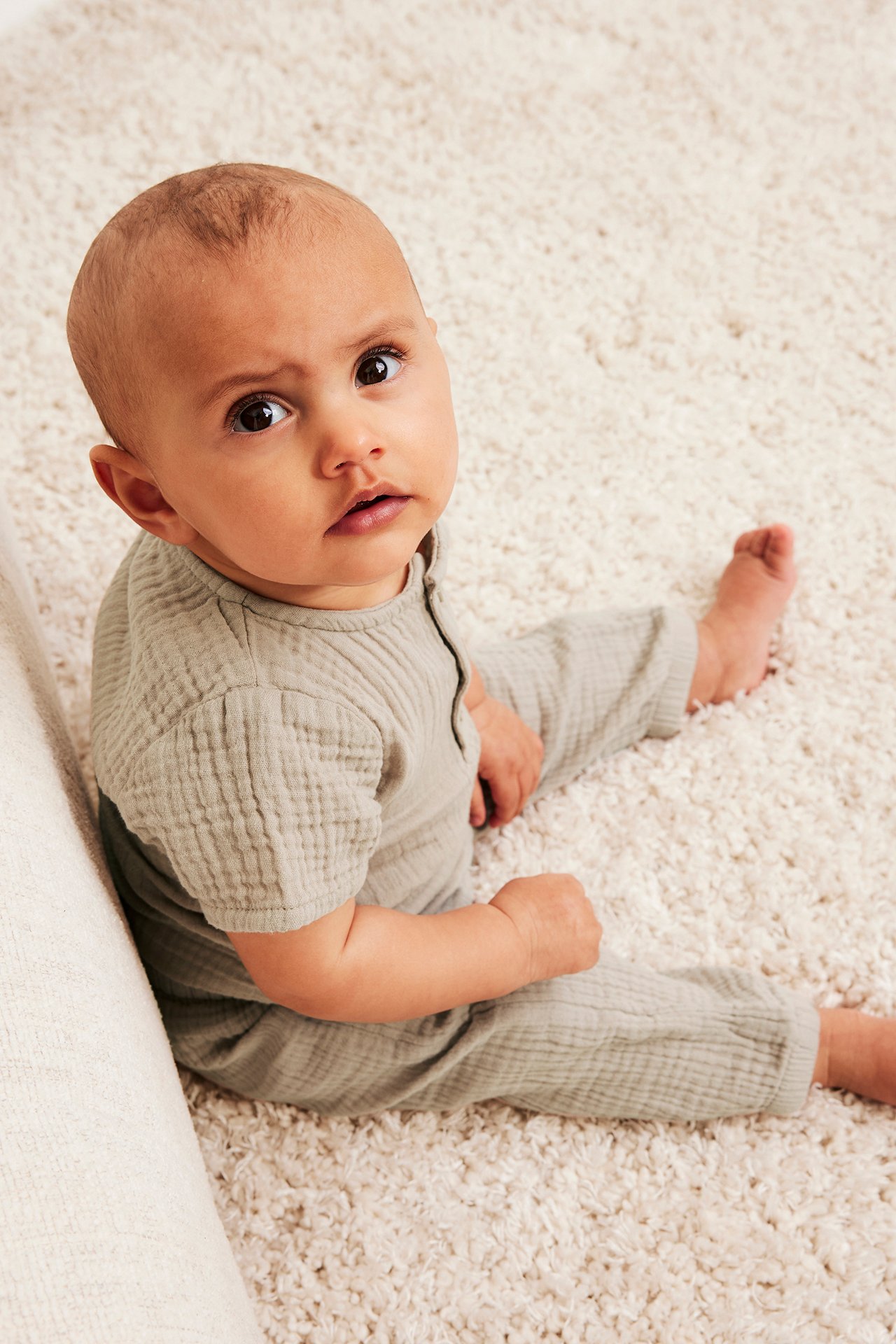 Framifrån, baby i ljusbeige muslinbyxor och matchande kortärmad topp.