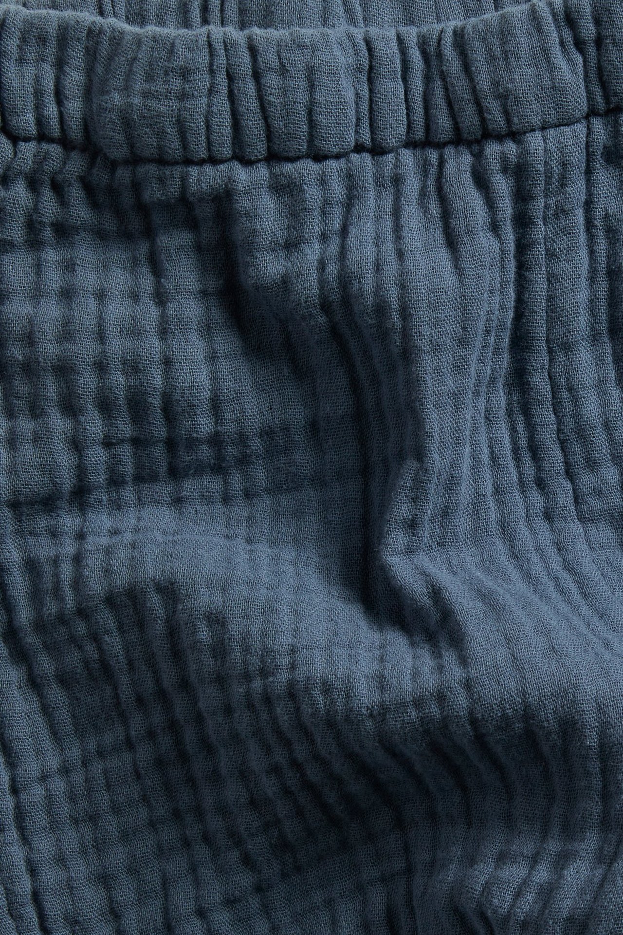 Nærbilde av blå muslinbukse som viser elastisk midjebånd og krøllet bomullsstoff.