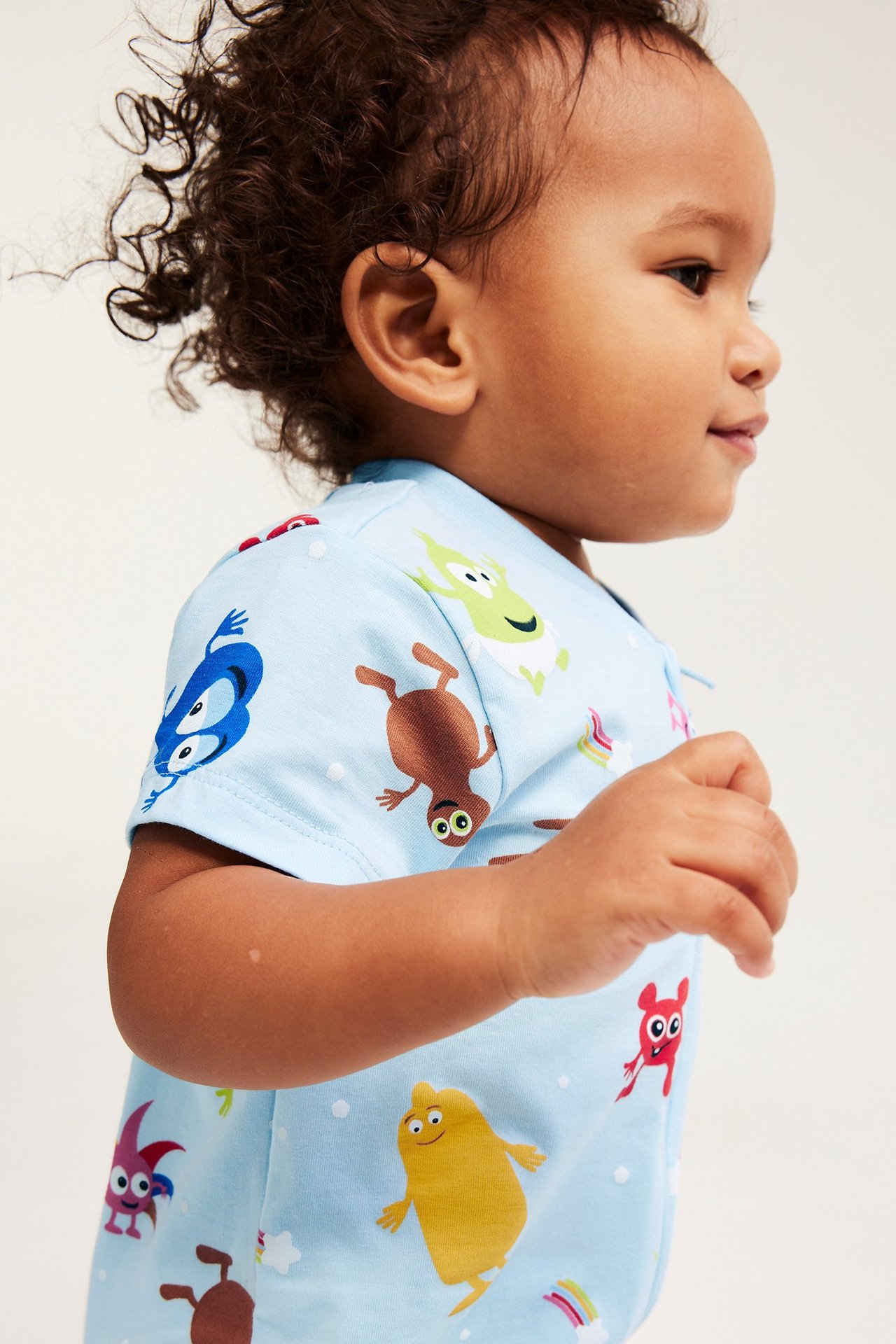 Sivukuva, vauva yllään vaaleansininen lyhythihainen Babblarna-haalari värikkäällä kuviolla ja yksisuuntaisella vetoketjulla.