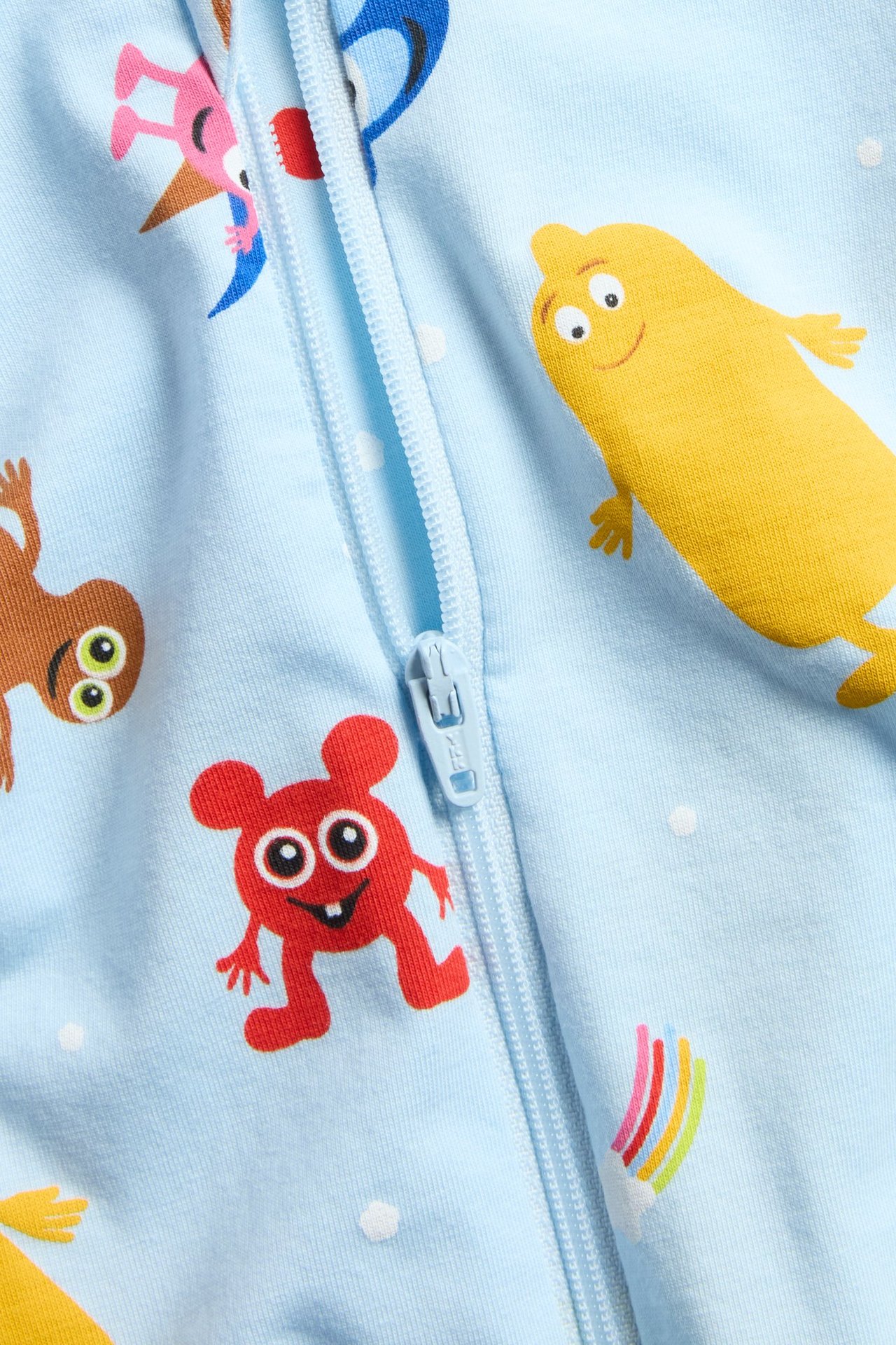 Lähikuva vauvan vaaleansinisestä Babblarna-kuvioidusta lyhythihaisesta haalaripyjamasta, jossa edessä vetoketju.