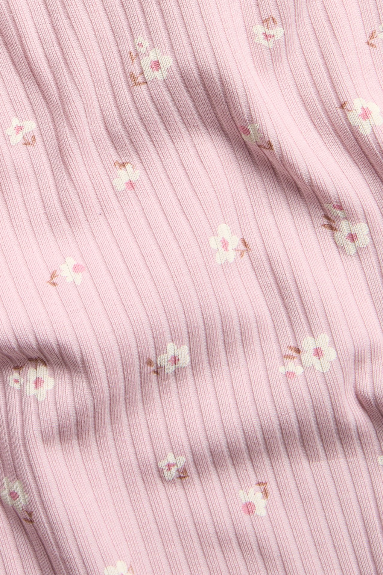Närbild av en ljusrosa ribbad kortärmad topp med ett blommigt minitryck.