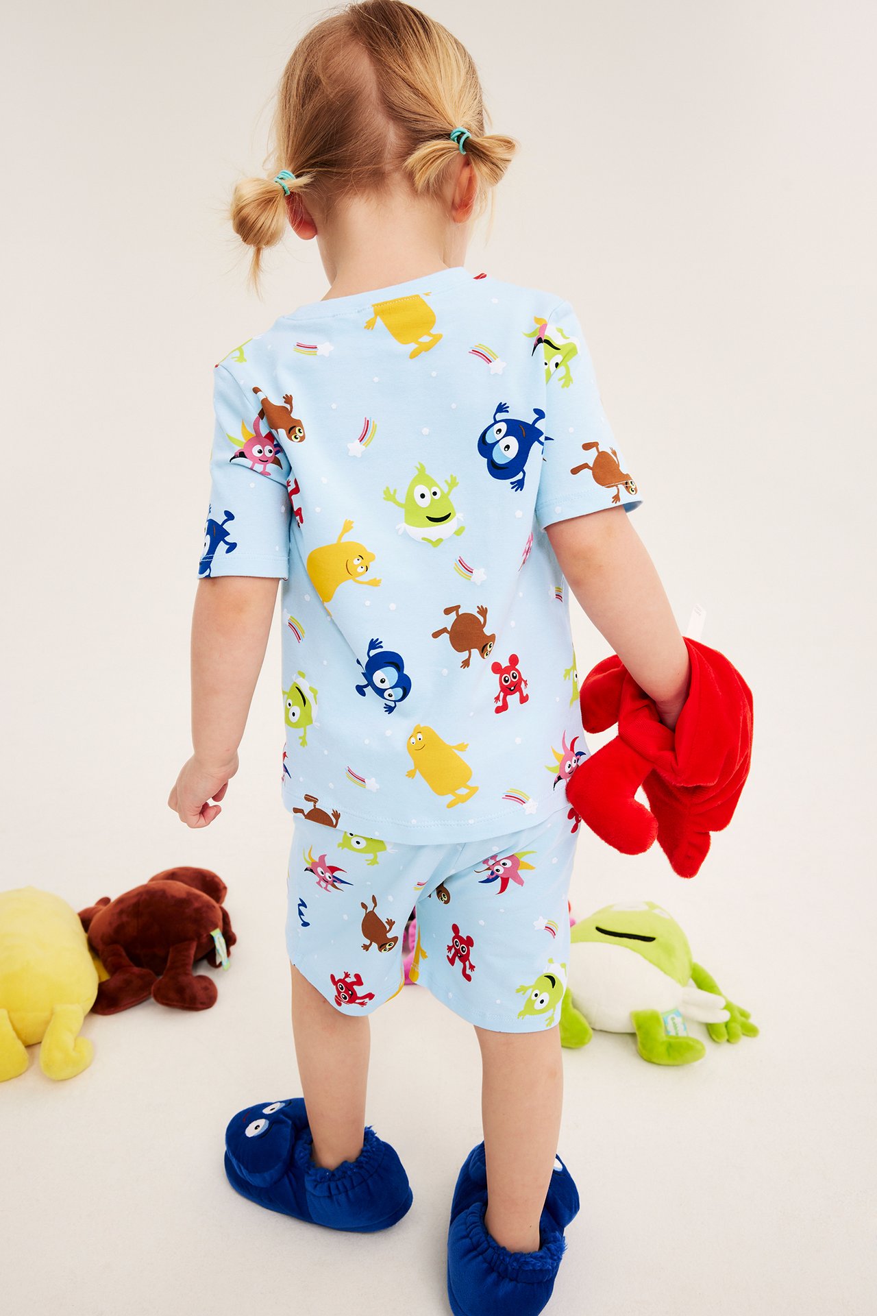 Bakifrån av ett barn i ett ljusblått Babblarna-mönstrat pyjamasset med shorts, håller en röd mjukdjursleksak.