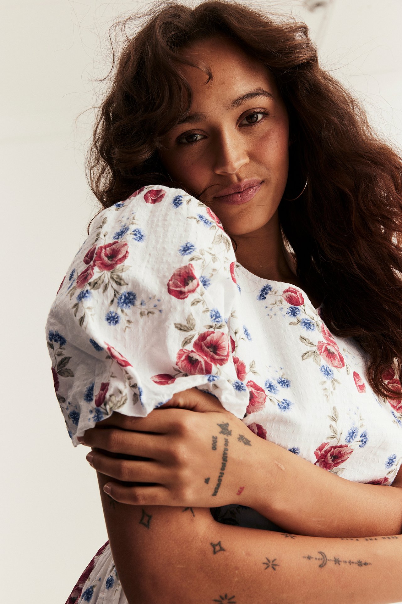 Lähikuva naisesta yllään luonnonvalkoinen kudottu kukkakuvioinen mekko punaisilla ja sinisillä kukilla ja pallohihoilla.