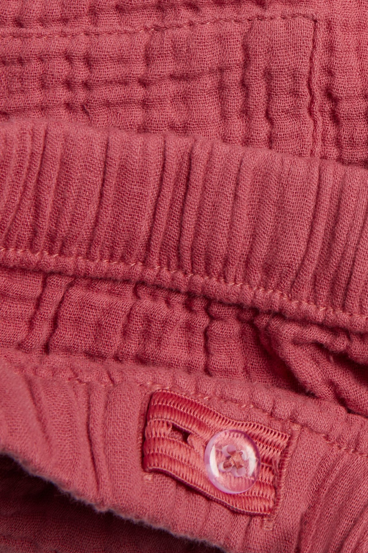 Zbliżenie na czerwone tkane bawełniane szorty z elastycznym pasem i regulowanym zapięciem na guzik.