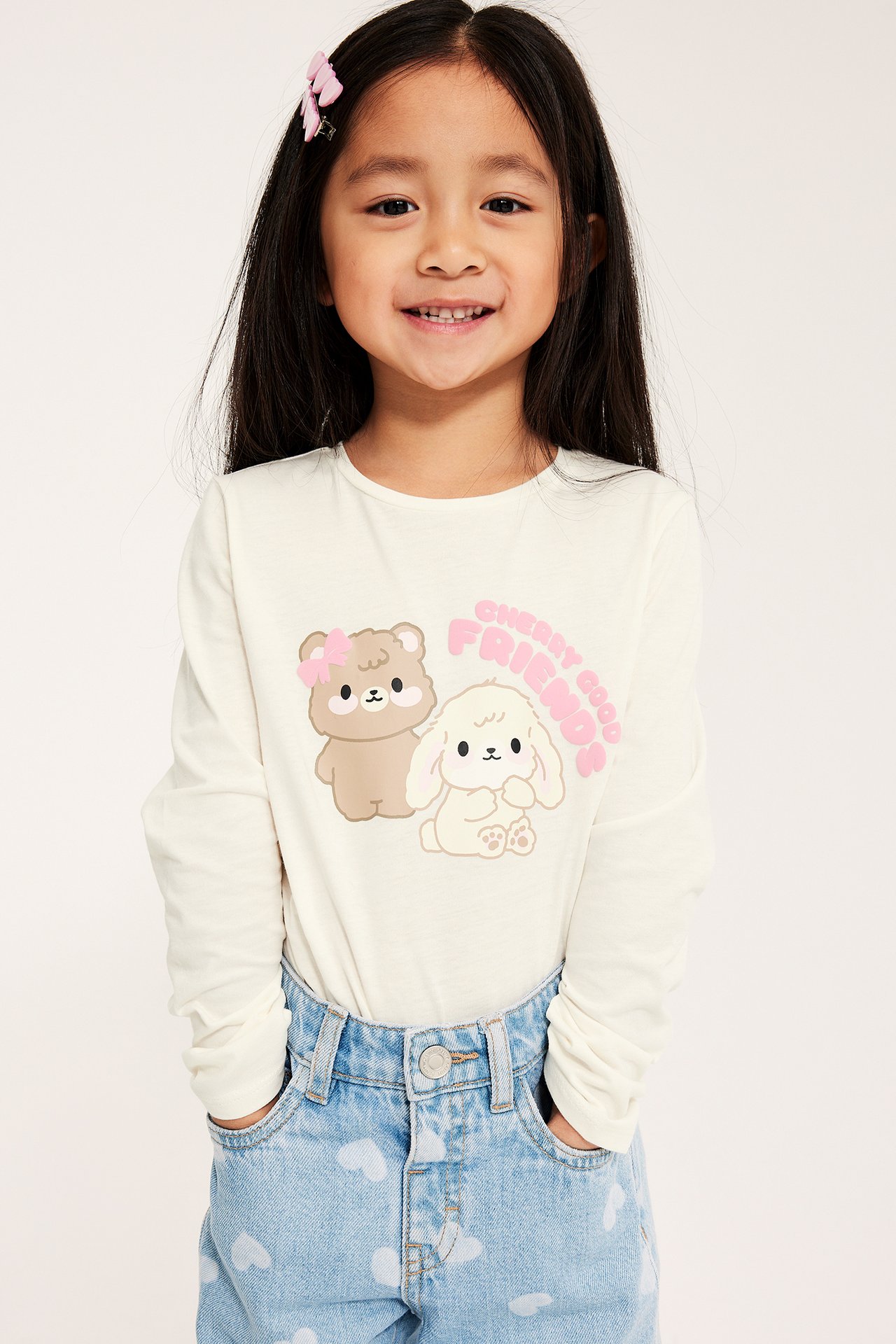 Lapsi, luonnonvalkoinen pitkähihainen paita eläinprintillä, vaaleansiniset sydänkuvioidut farkut ja vaaleanpunaiset hiusklipsit.