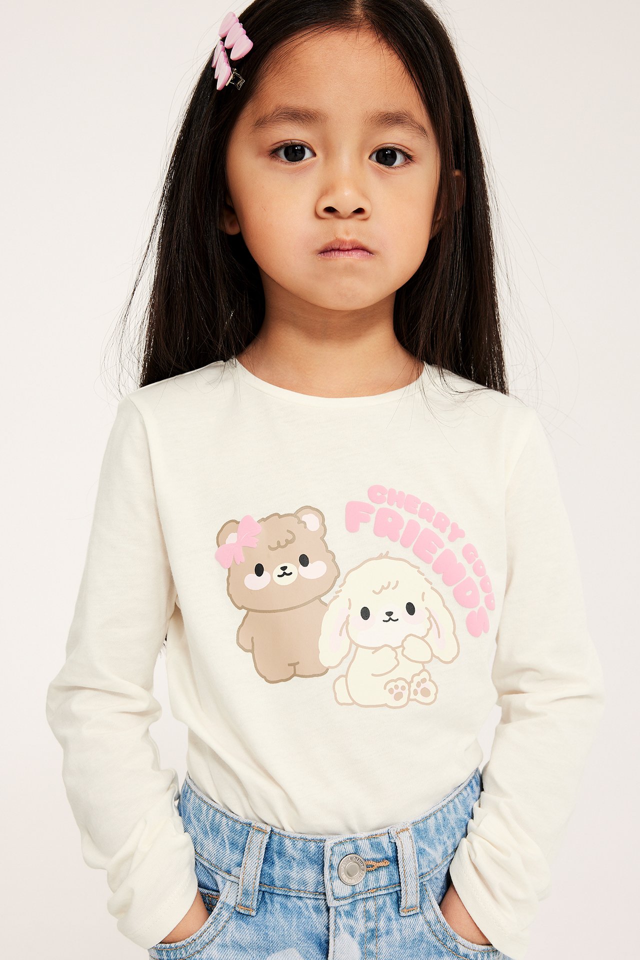 Forfra: Barn i offwhite langermet bomullstopp med bjørn- og kanintrykk, blå jeans, og rosa hårspenne.