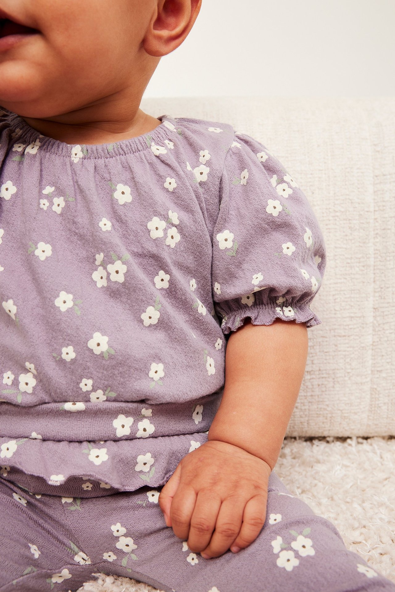 Närbild på baby i lila blommig crepe-body med puffärmar och matchande byxor.